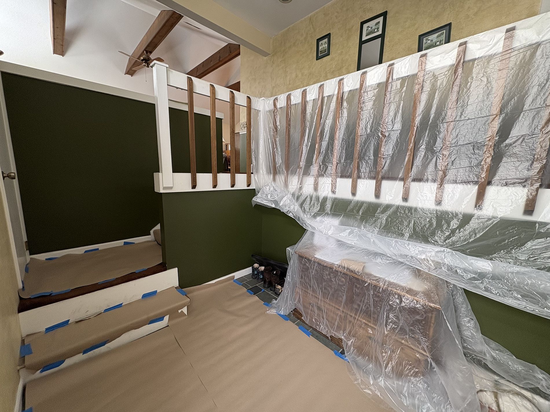 Stairwell and landing with green walls, white railing, and furniture wrapped in plastic