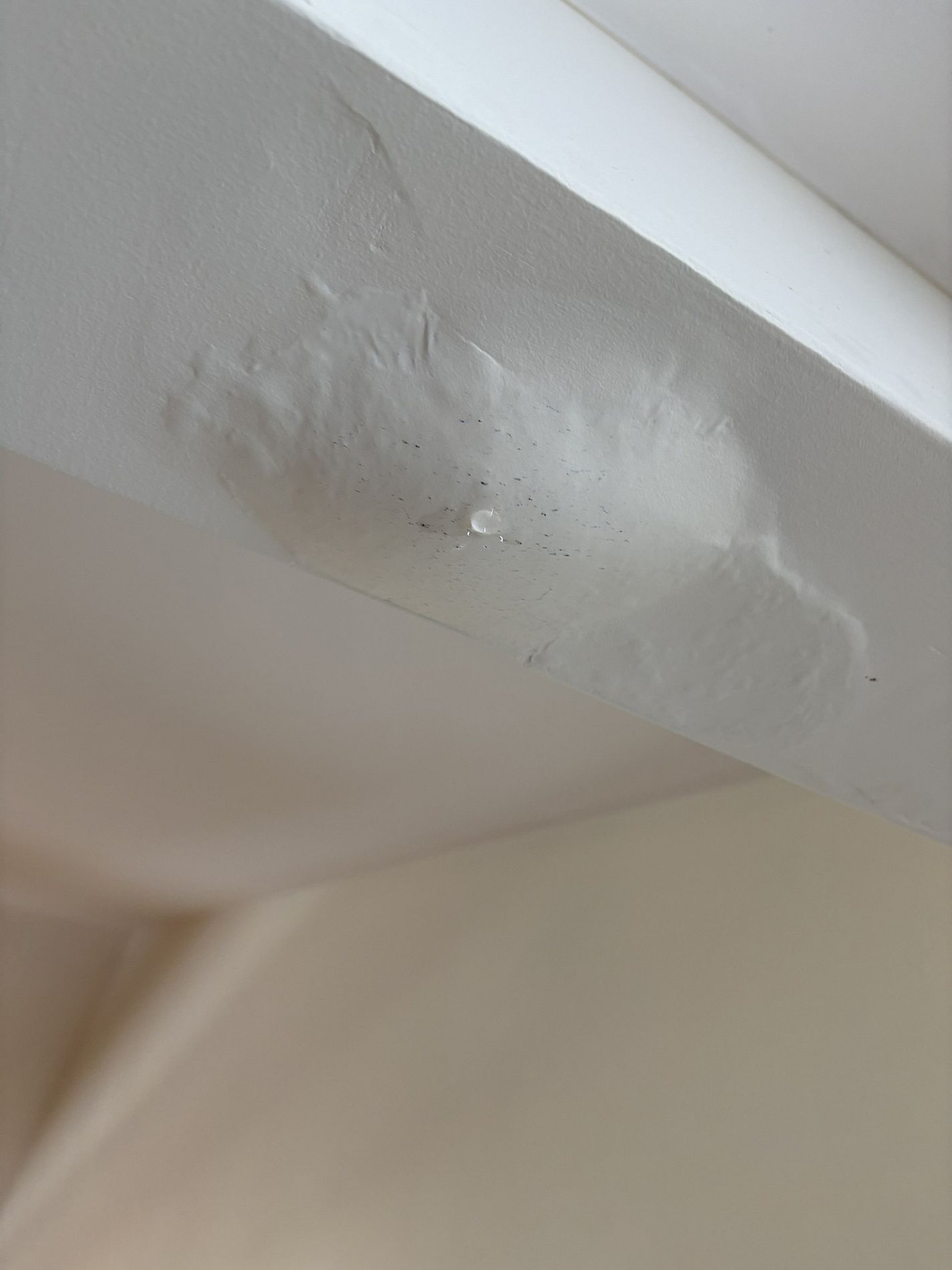 White ceiling beam with peeling, bubbled paint damage near the corner