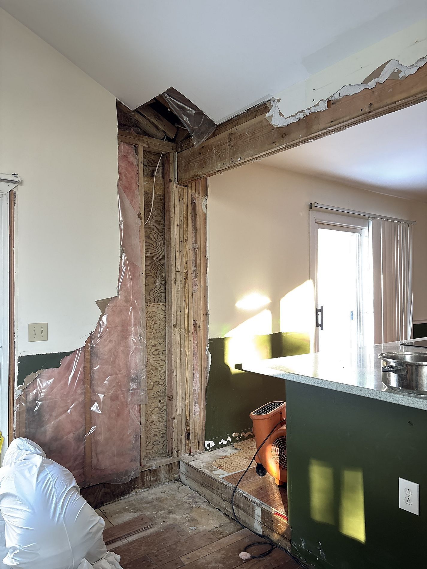 Interior room under renovation with exposed wooden framing and damaged wall plaster near a window and sink.