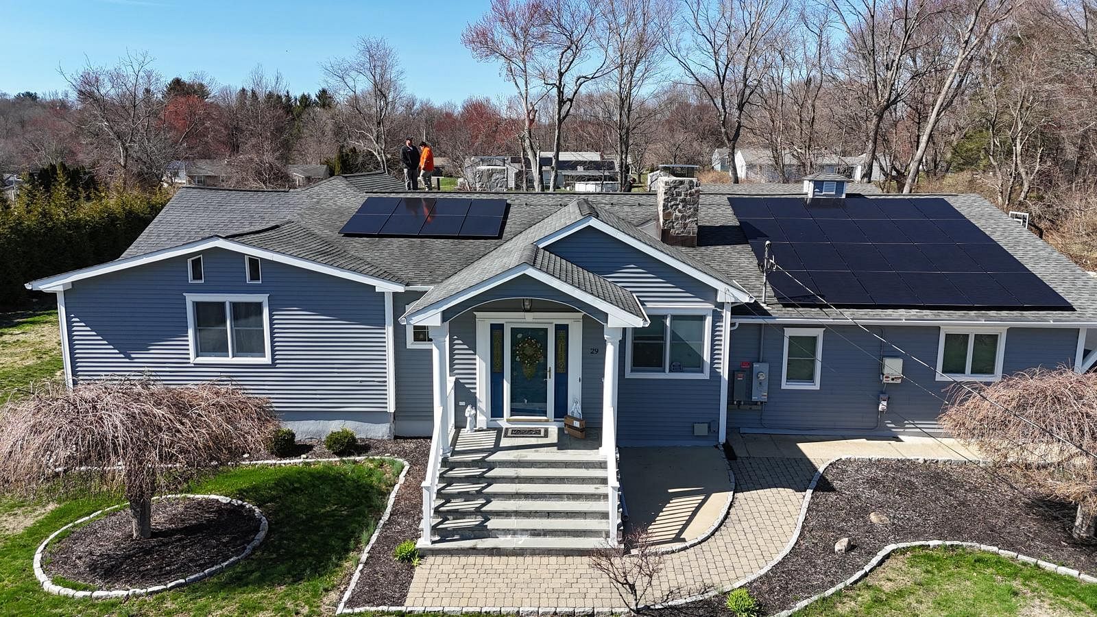 Gray single-story house with front steps, black roof, solar panels, and a landscaped yard
