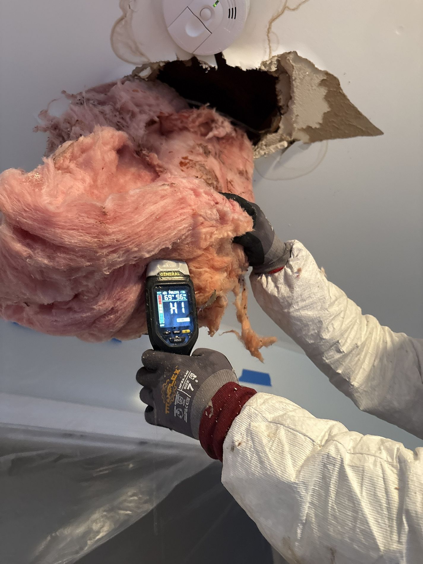 Worker inspecting exposed ceiling insulation with a handheld thermal camera