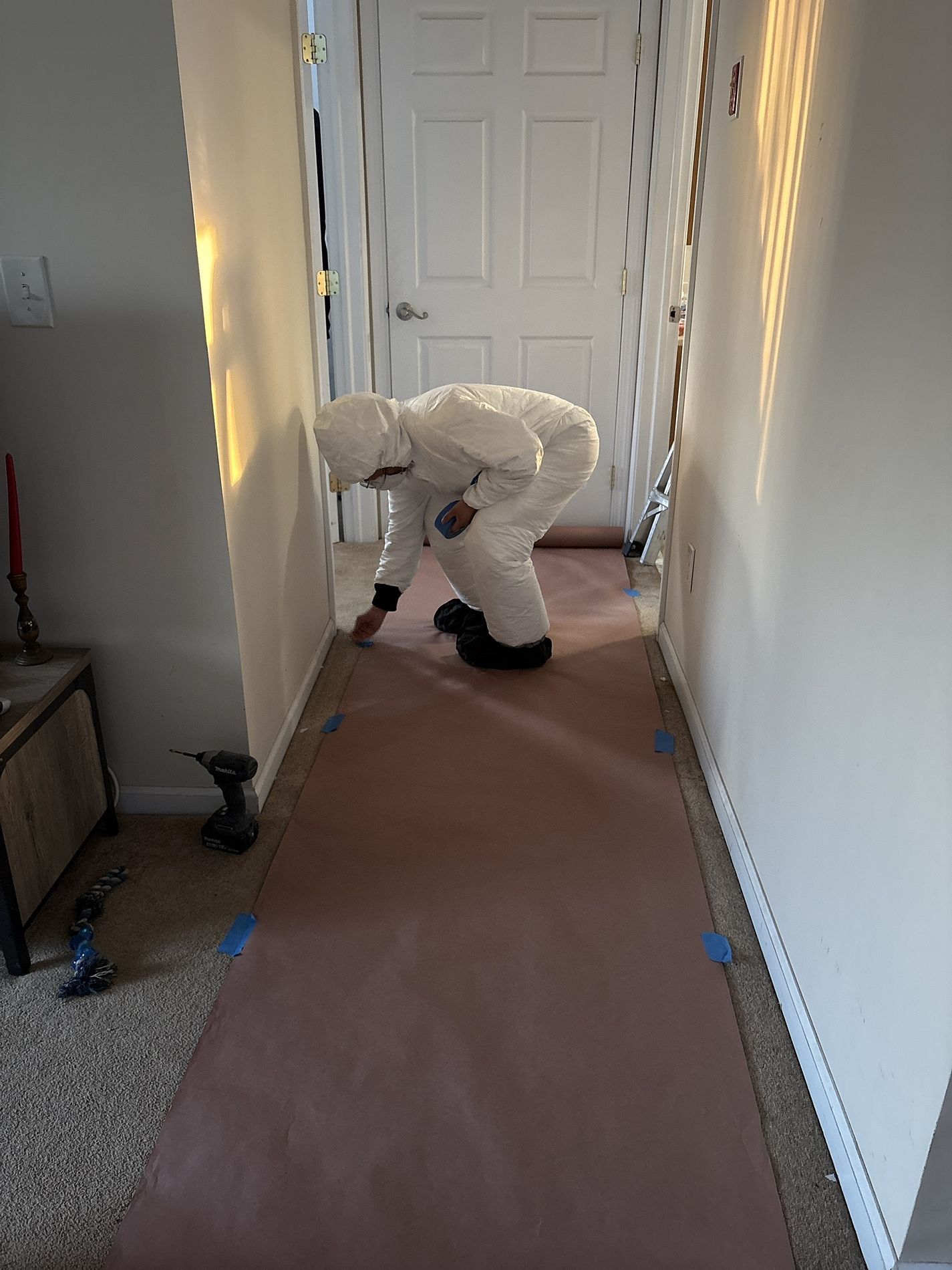 Person in white coveralls vacuuming a hallway with brown carpet protectant.