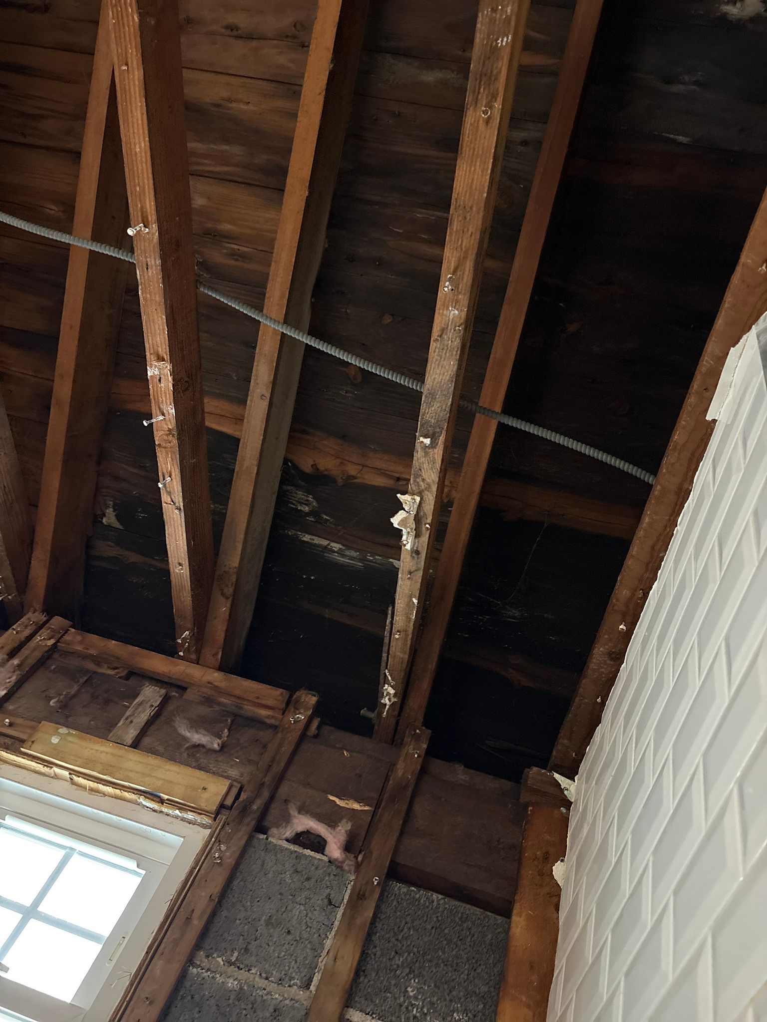 Exposed wooden ceiling beams above a window and white brick wall in a room