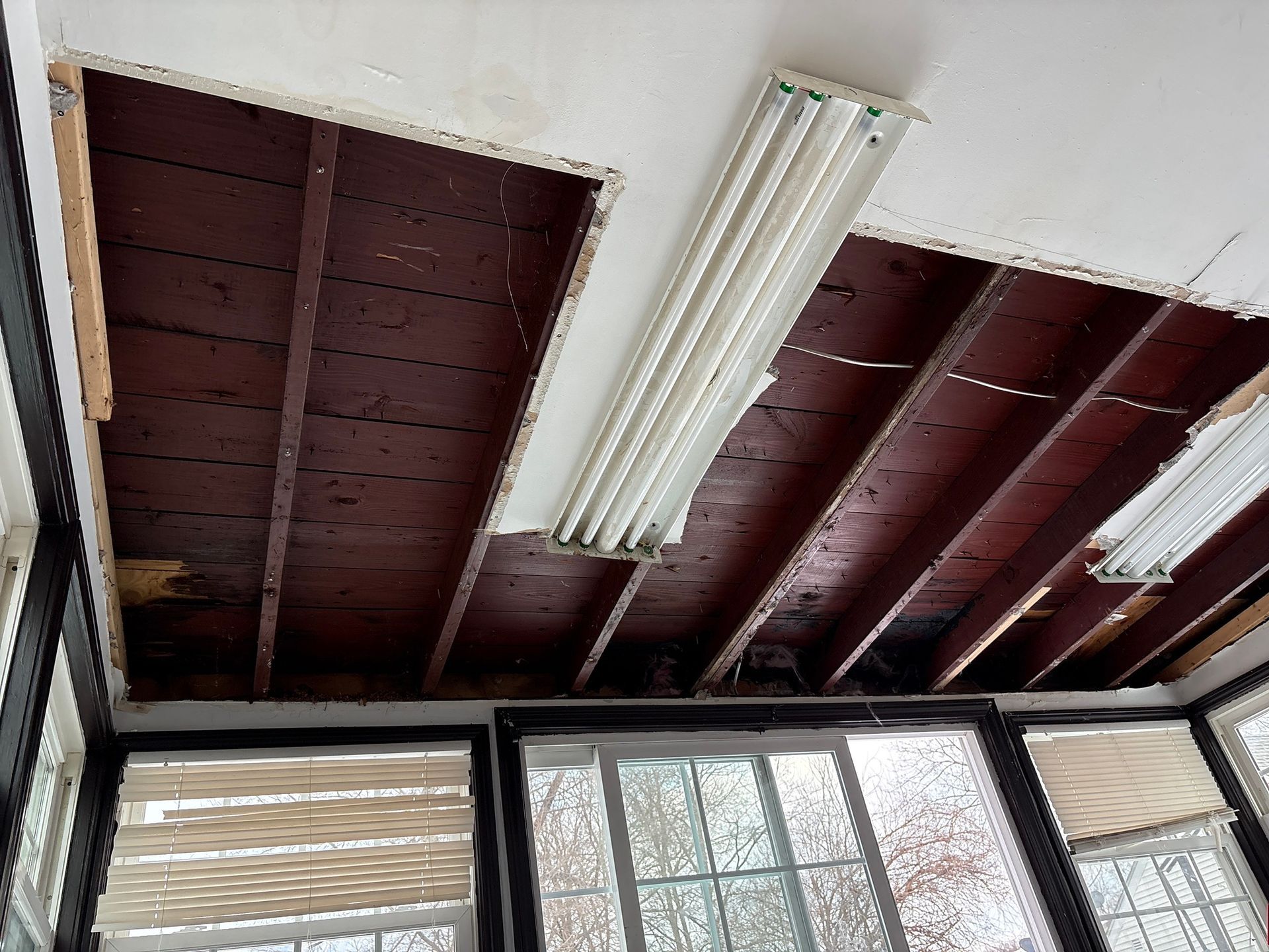 Exposed wooden ceiling with fluorescent light fixture above windows and blinds
