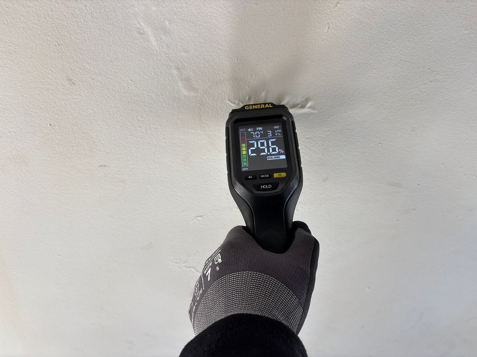 Handheld thermal camera aimed at a white wall, showing a heat reading on the screen