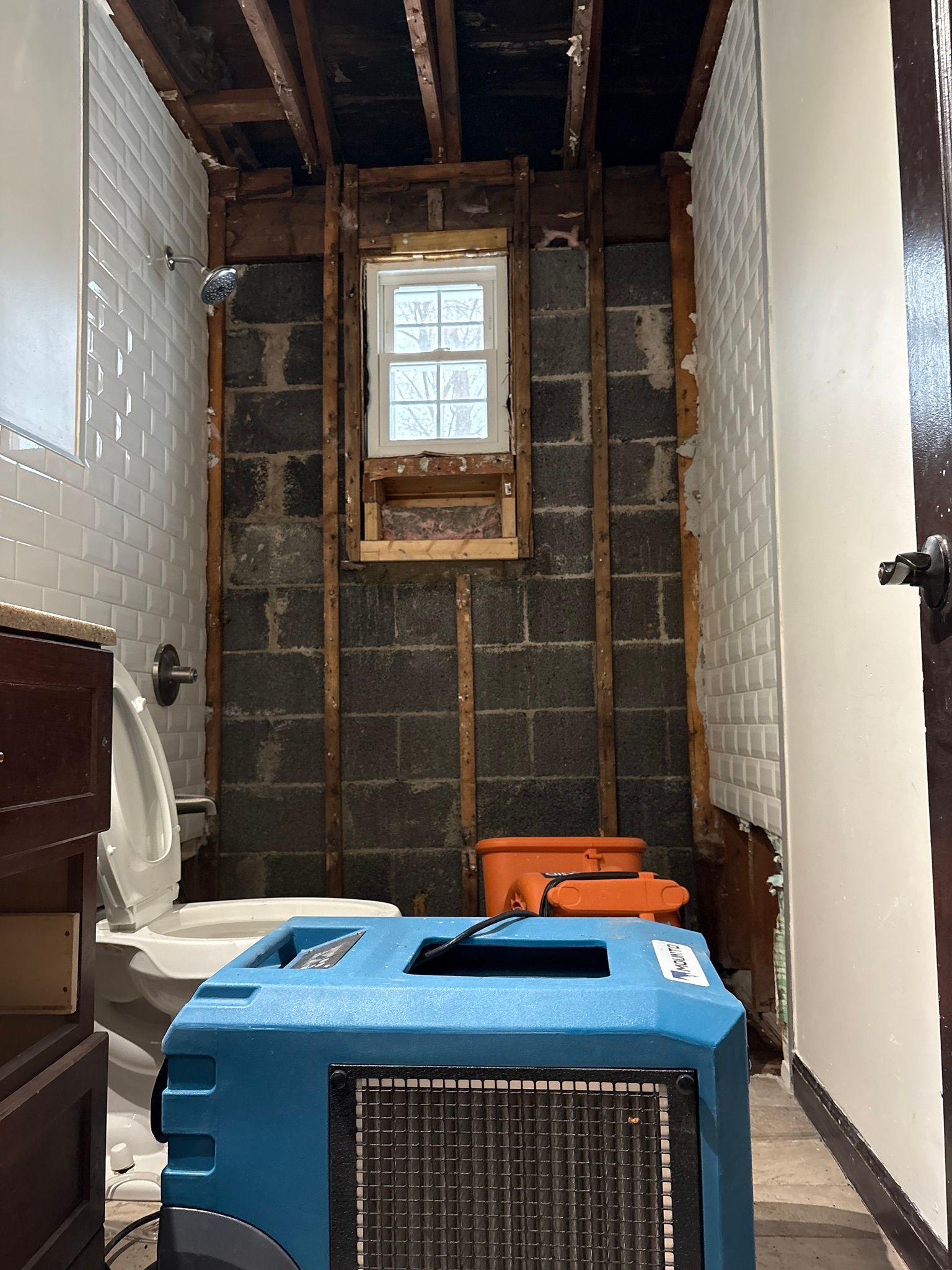 Renovation site with exposed walls, a small window, and a blue portable machine in the foreground