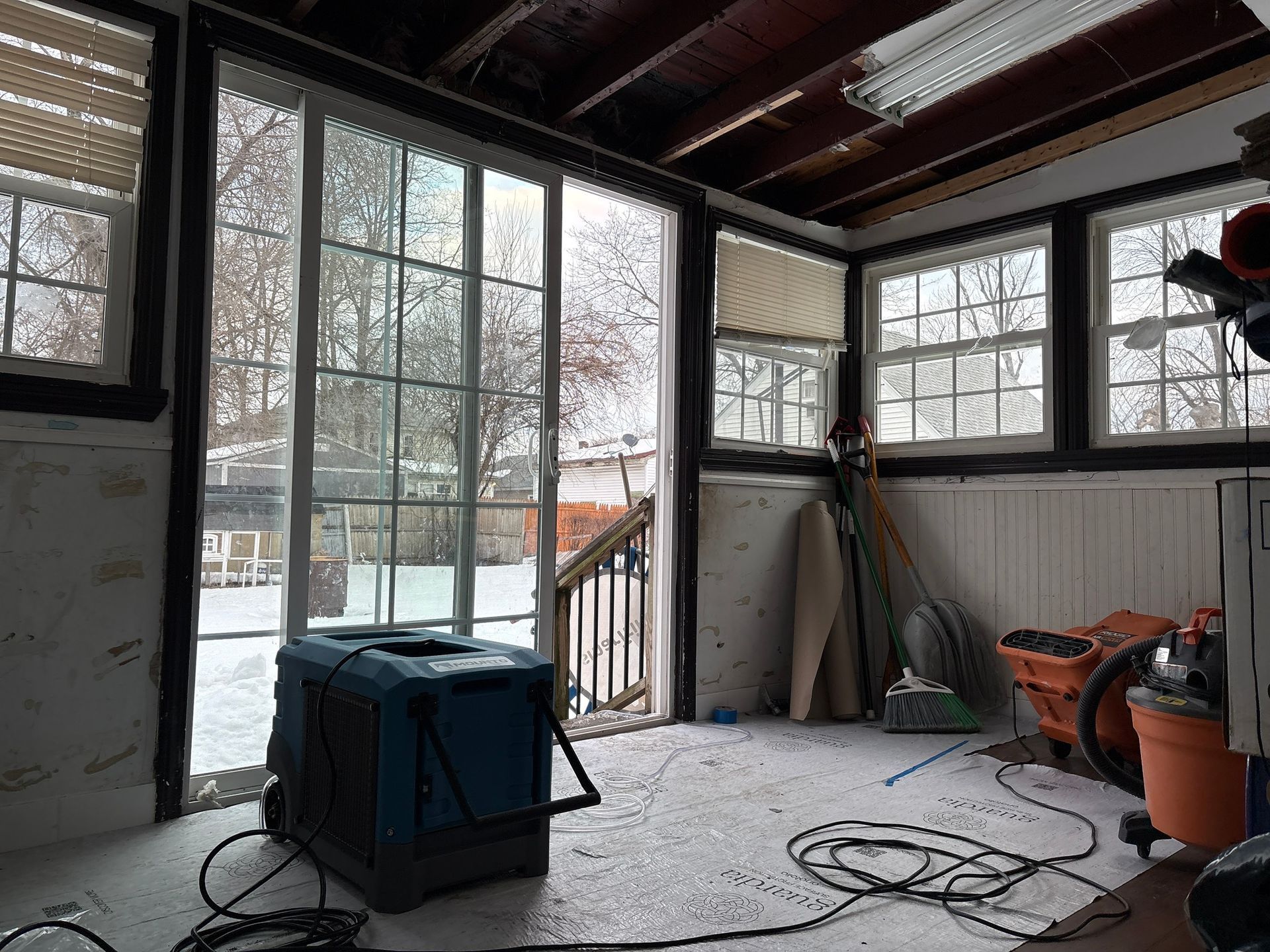 Snowy porch or garage with large windows, a blue storage bin, and tools on the floor