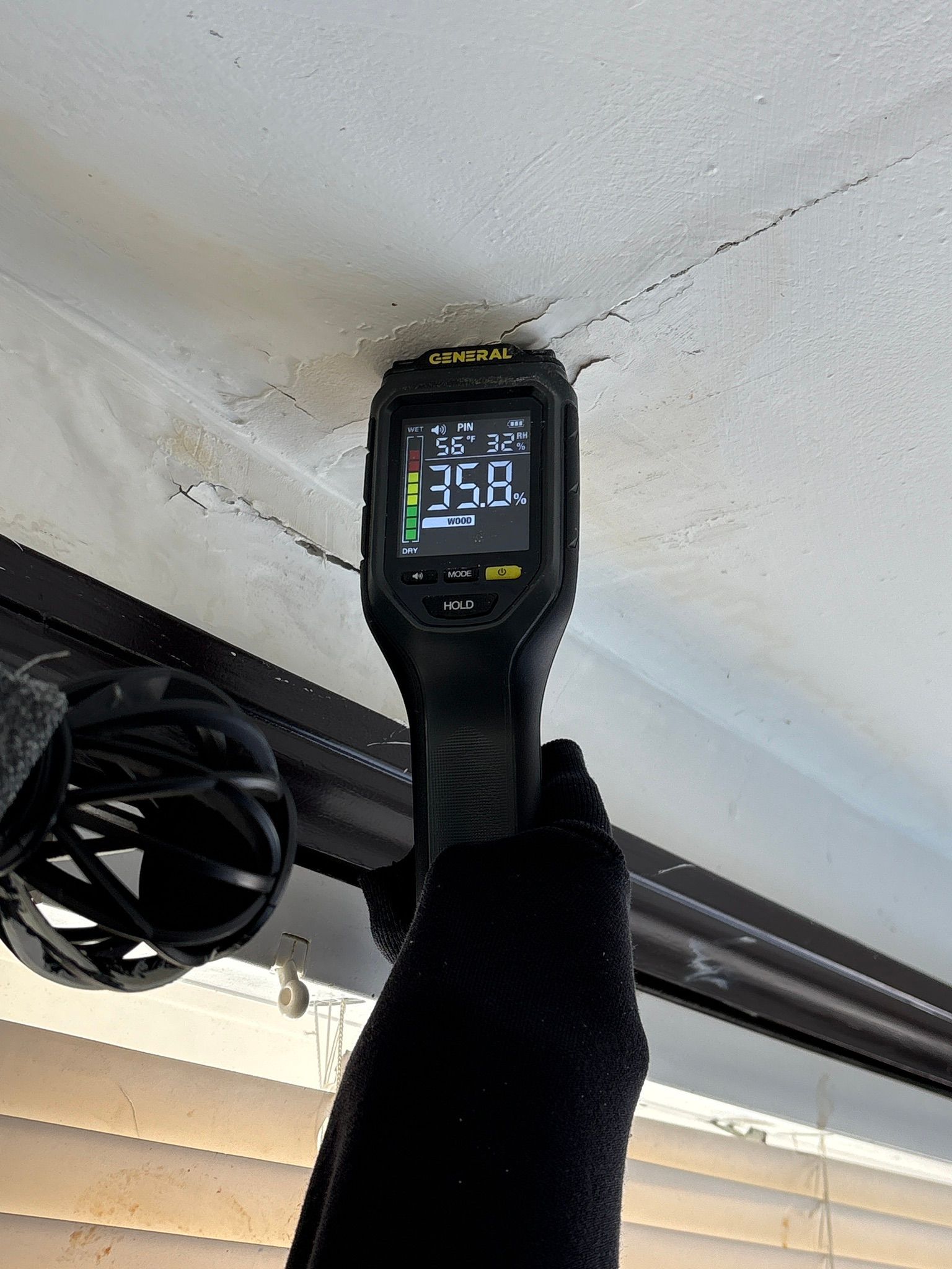 Black smartwatch with a lit screen mounted on a black strap under a white ceiling near a fan.