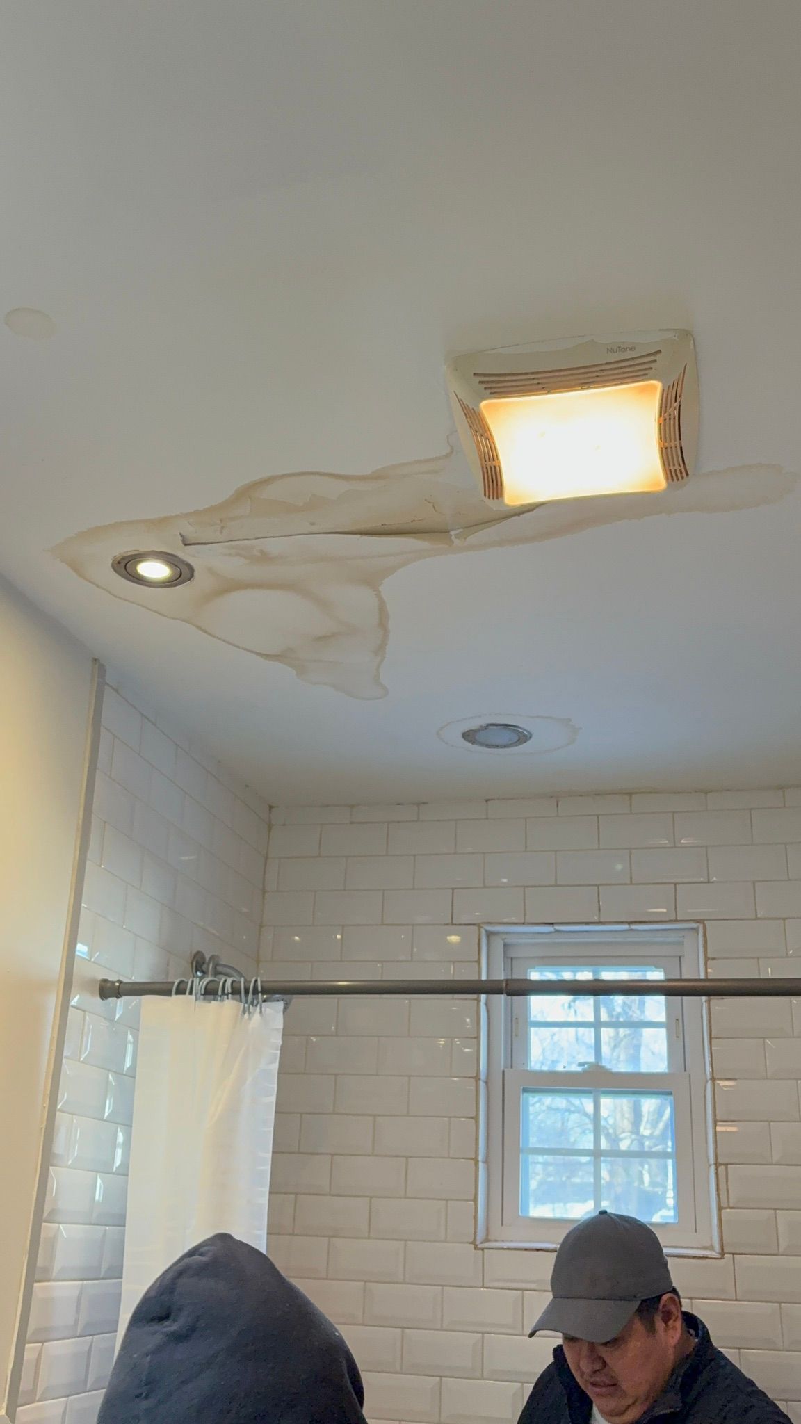 Bathroom ceiling with water stains, a damaged light fixture, and a tiled shower area below.