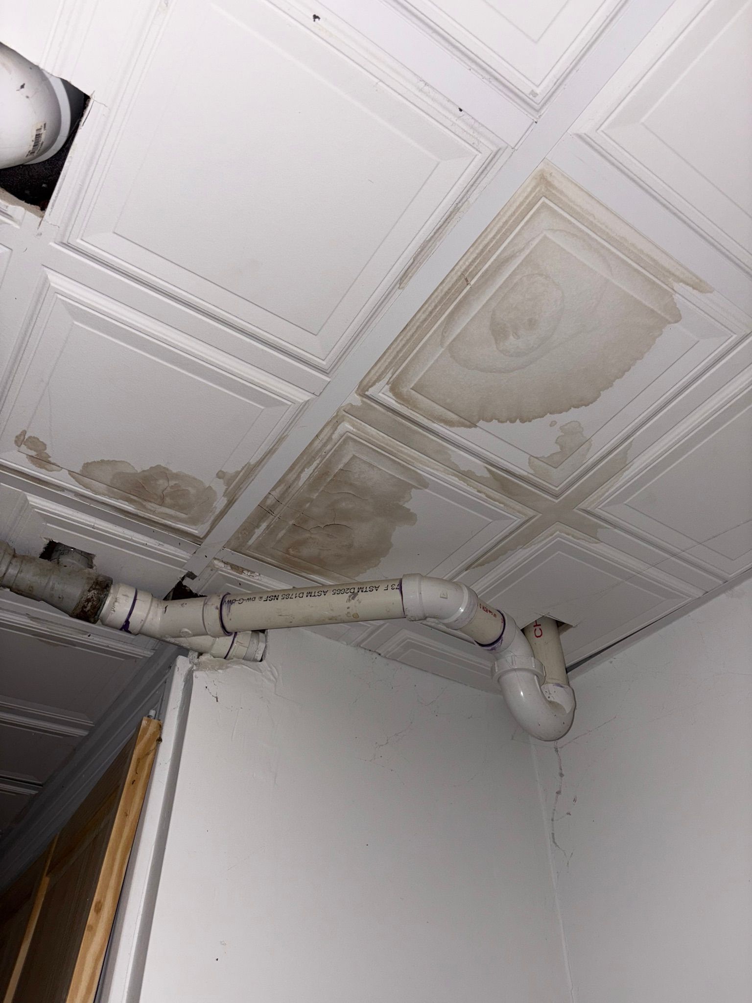 Ceiling with water stains and exposed pipes in a corner of a room