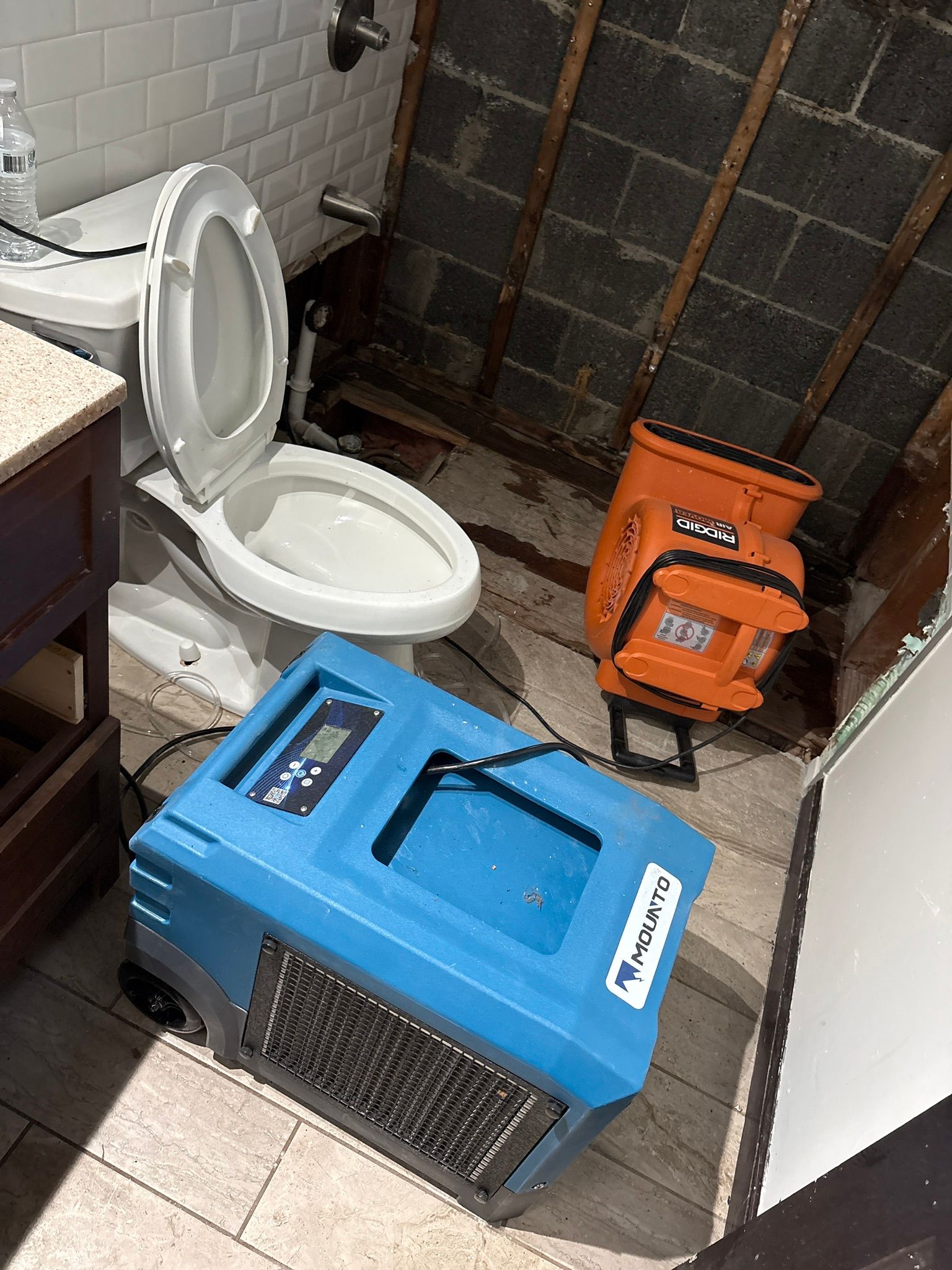 Small bathroom with an open toilet and two portable dehumidifiers, one blue and one orange.