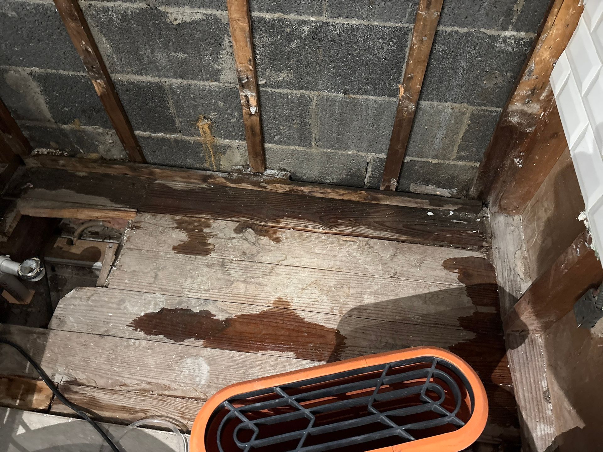 Damp basement corner with water stains on a concrete wall and floor, plus a small orange heater or fan.
