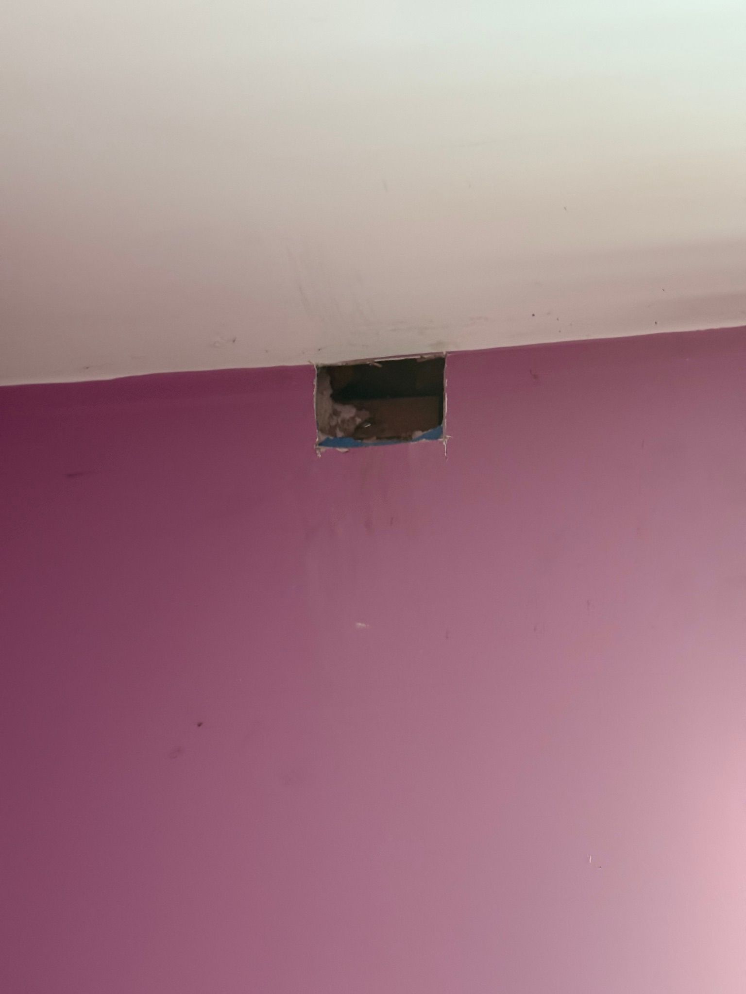 Pink wall with a small open hole near the ceiling and exposed dark interior
