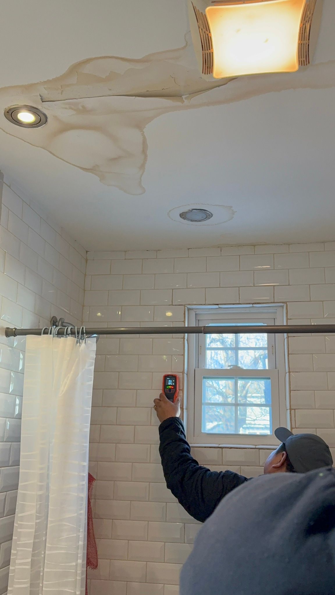 Person holding up a phone while photographing a bathroom ceiling leak and water damage