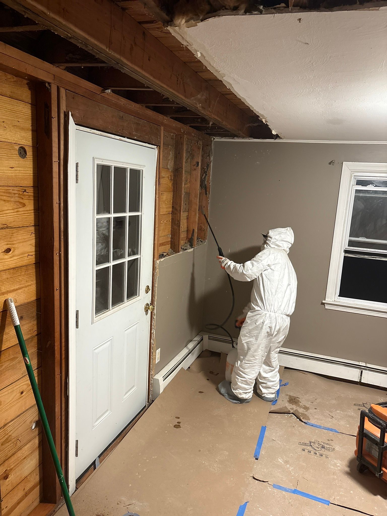 Worker painting unfinished room with sprayer near a white door and gray walls