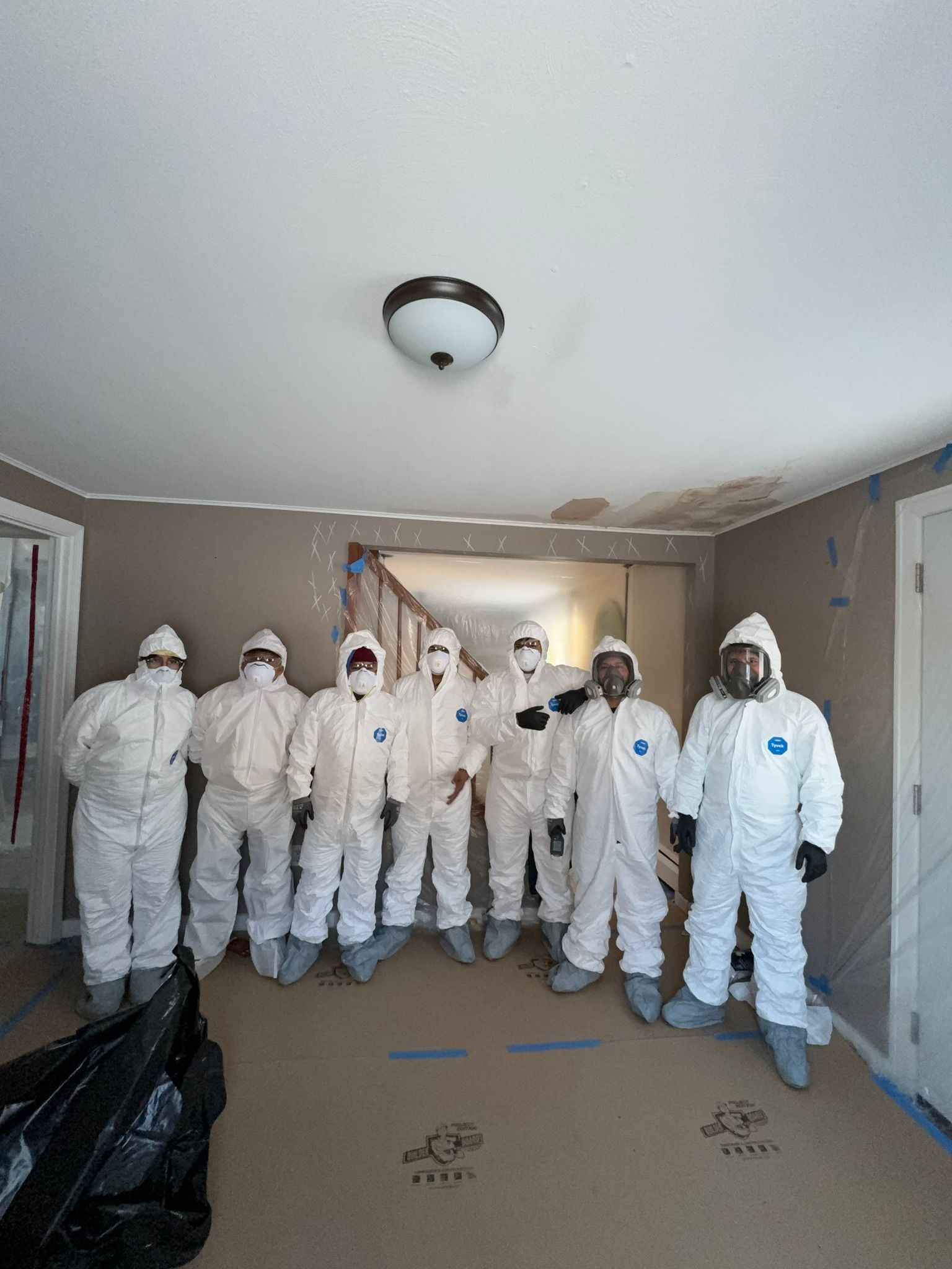 Group of people in white protective suits and masks standing in a hallway at a cleanup site