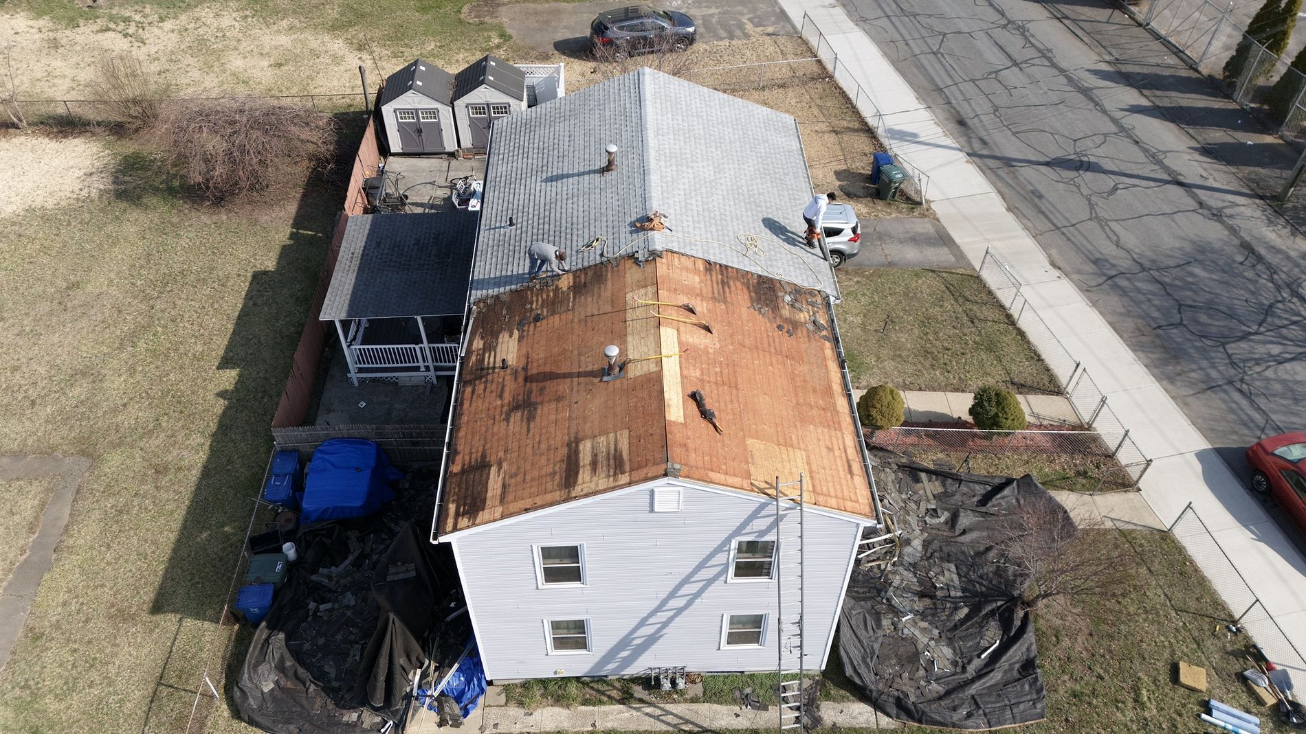 Aerial view of a house with a rusted metal roof, surrounded by yard and driveway.