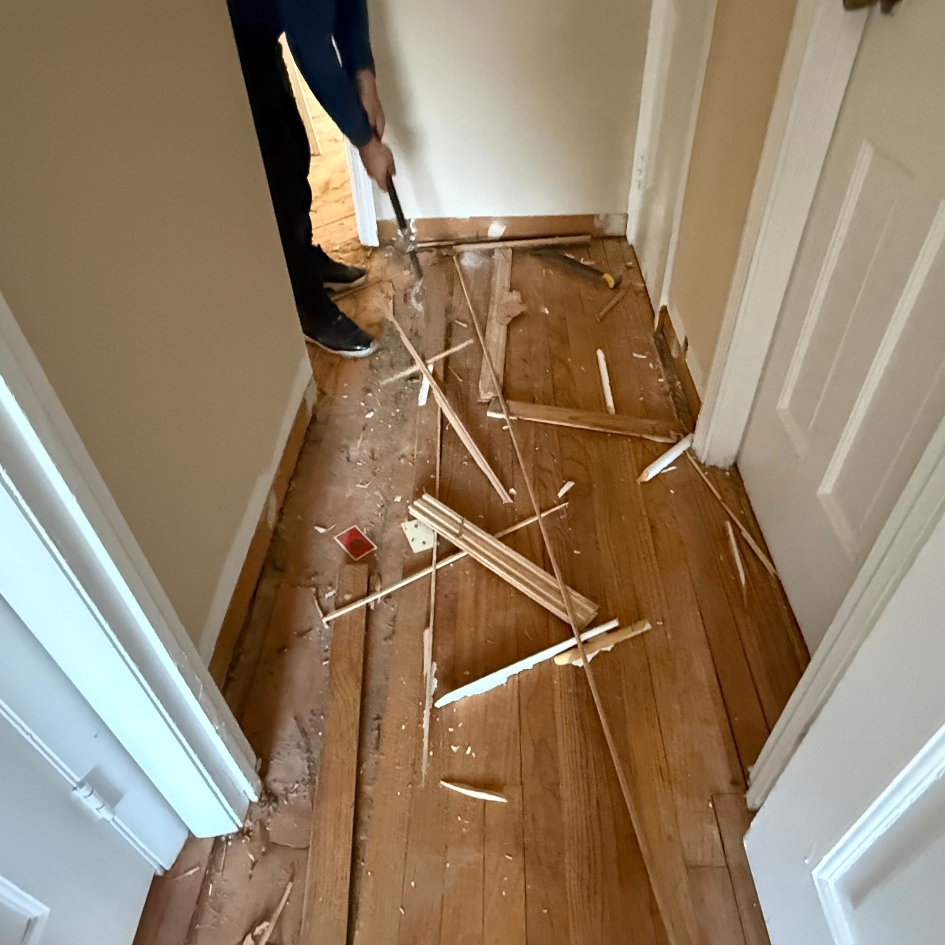 Broken wooden slats scattered across a hallway floor as a person sweeps debris
