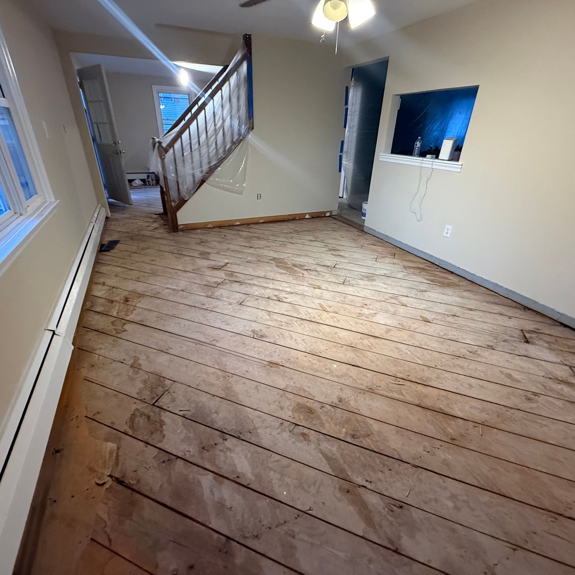 Empty room with wide-plank wood floors, staircase, and a small pass-through window in the wall