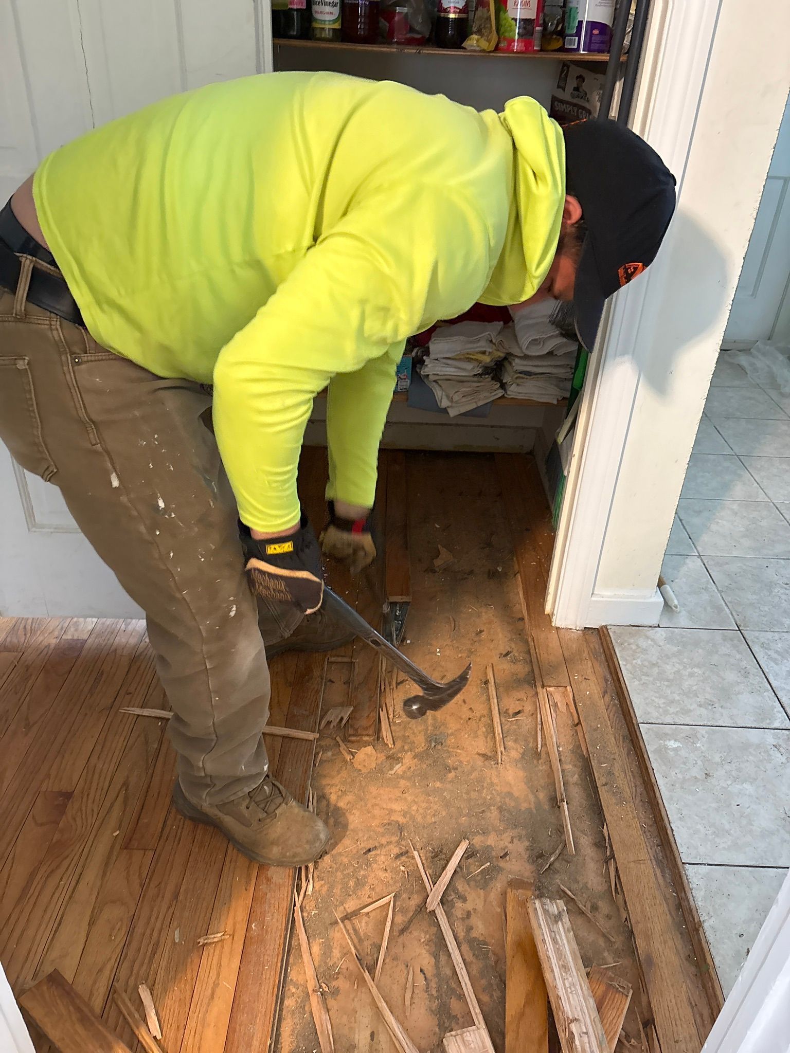 Worker in neon yellow hoodie removing flooring with a pry bar in a doorway.