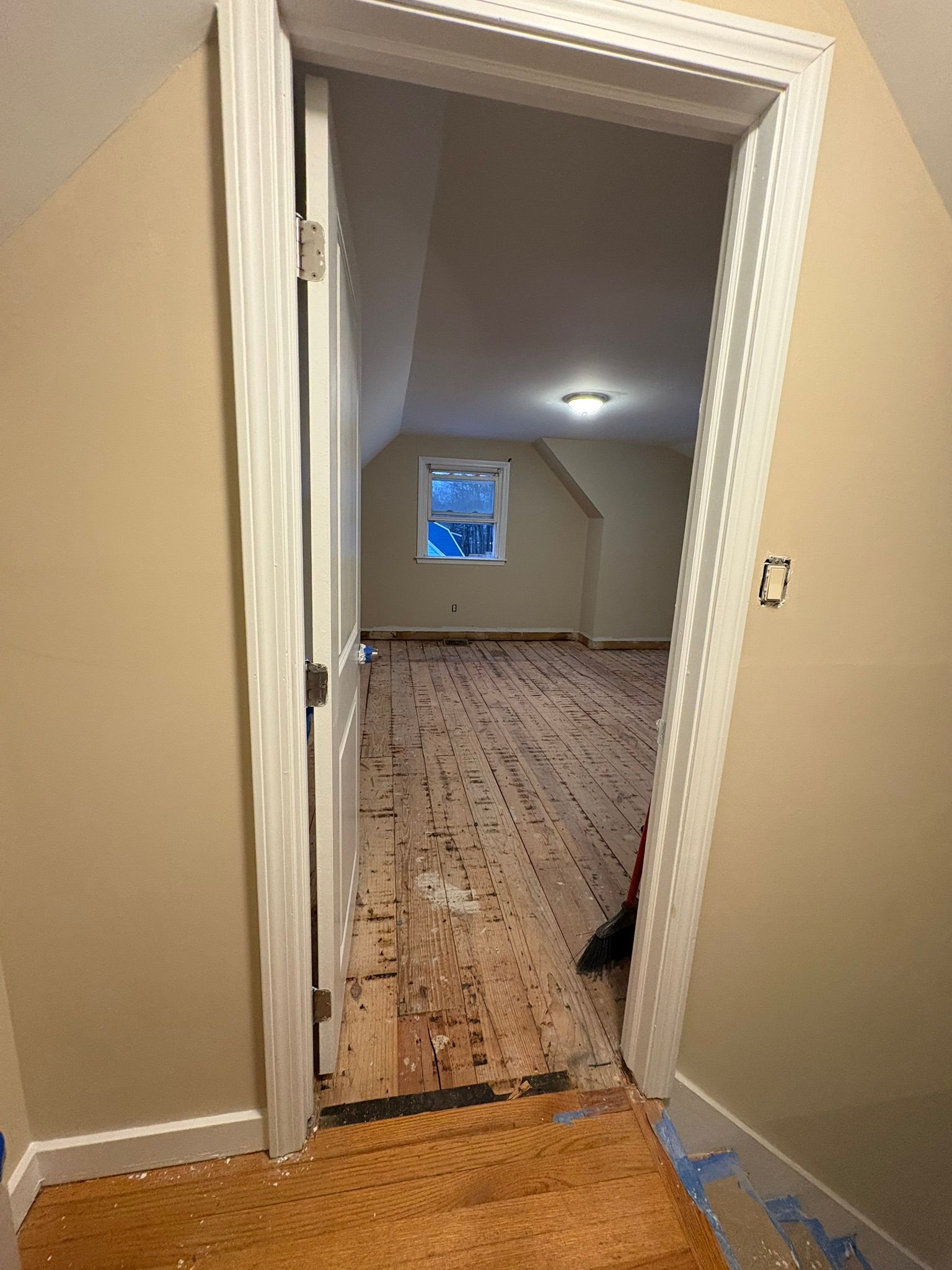 Open doorway to a sparsely furnished room with bare subfloor and a small window.