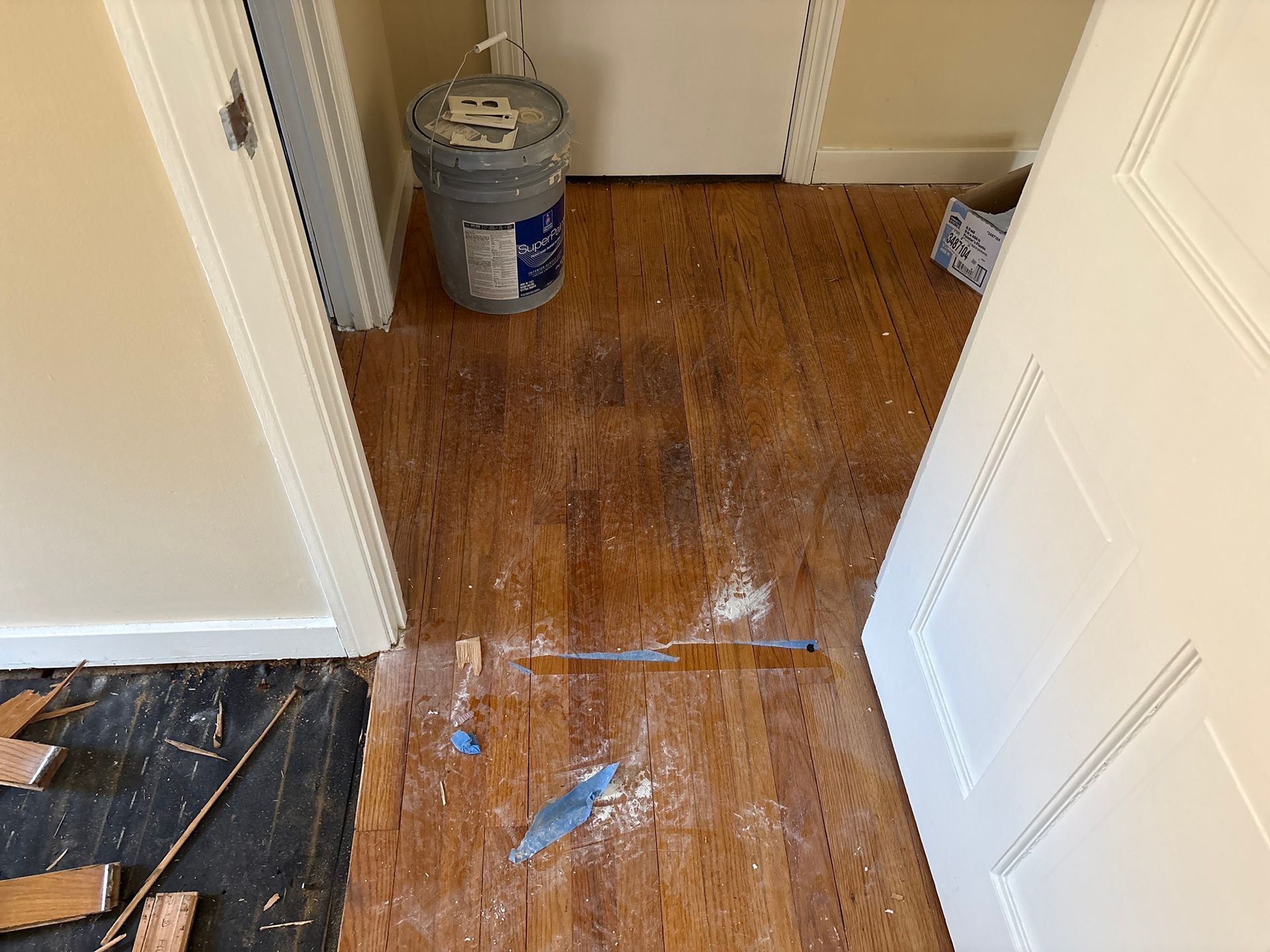 Partially repaired hallway floor with exposed subfloor and paint buckets near a white door