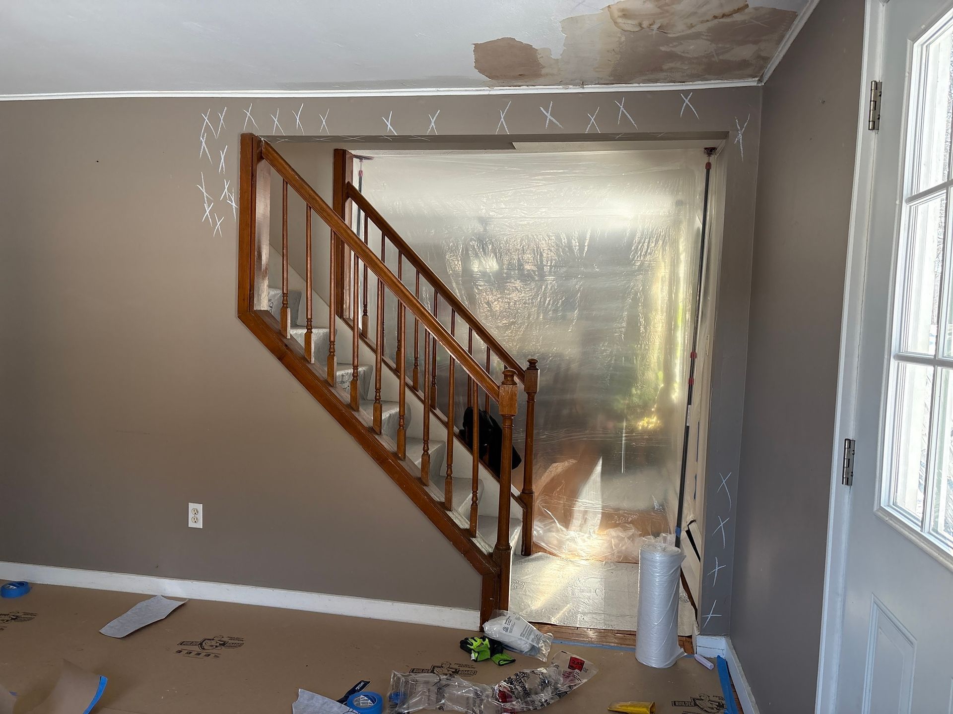 Partially renovated room with wooden staircase, gray walls, and plastic sheeting over a doorway