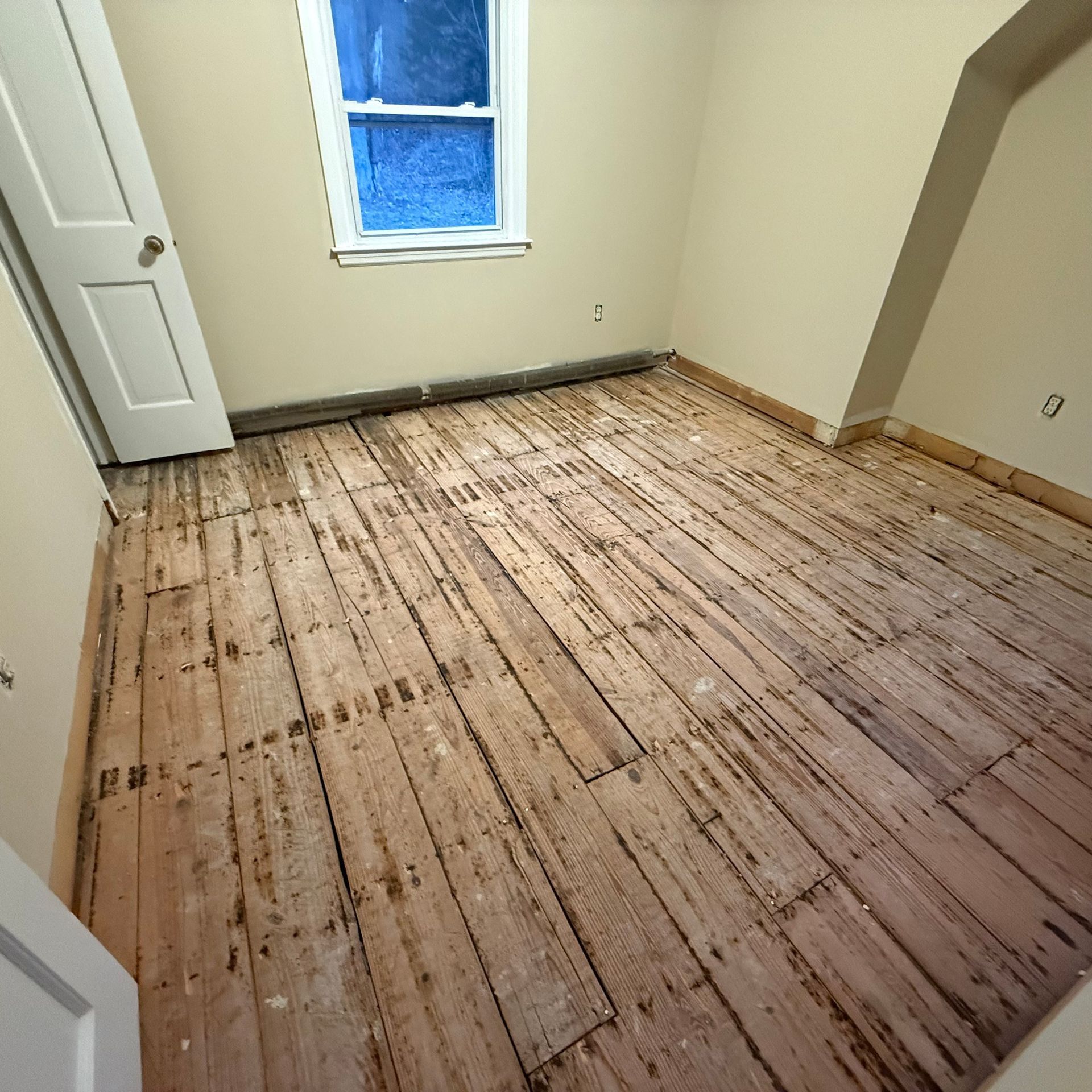 Empty room with bare wooden floor, beige walls, and a small window.