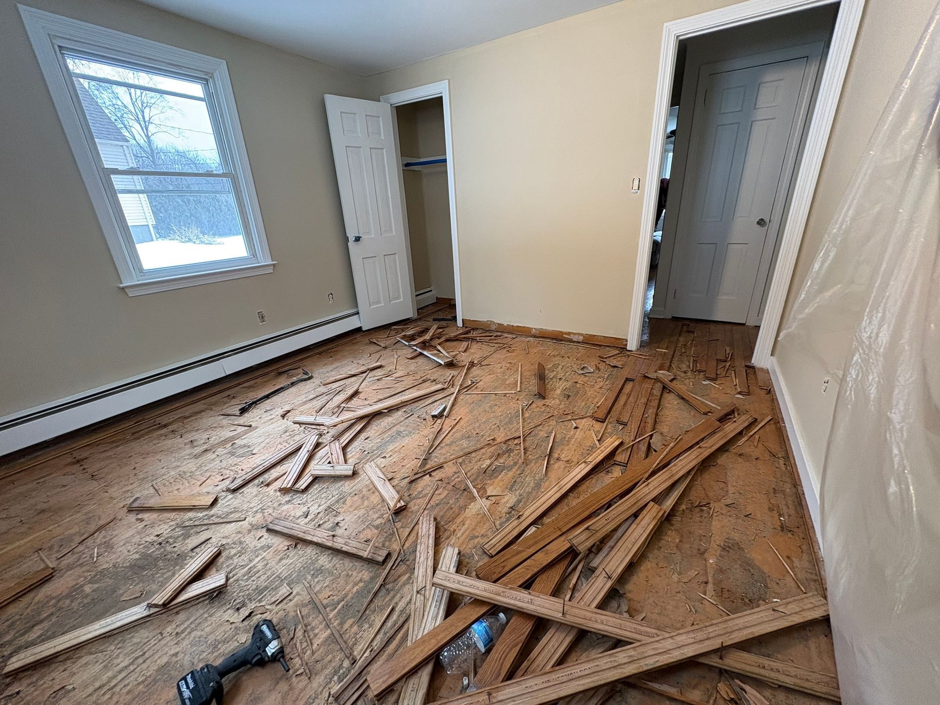 Room under renovation with debris and torn flooring on the floor, open closets, and a window with a radiator beneath it