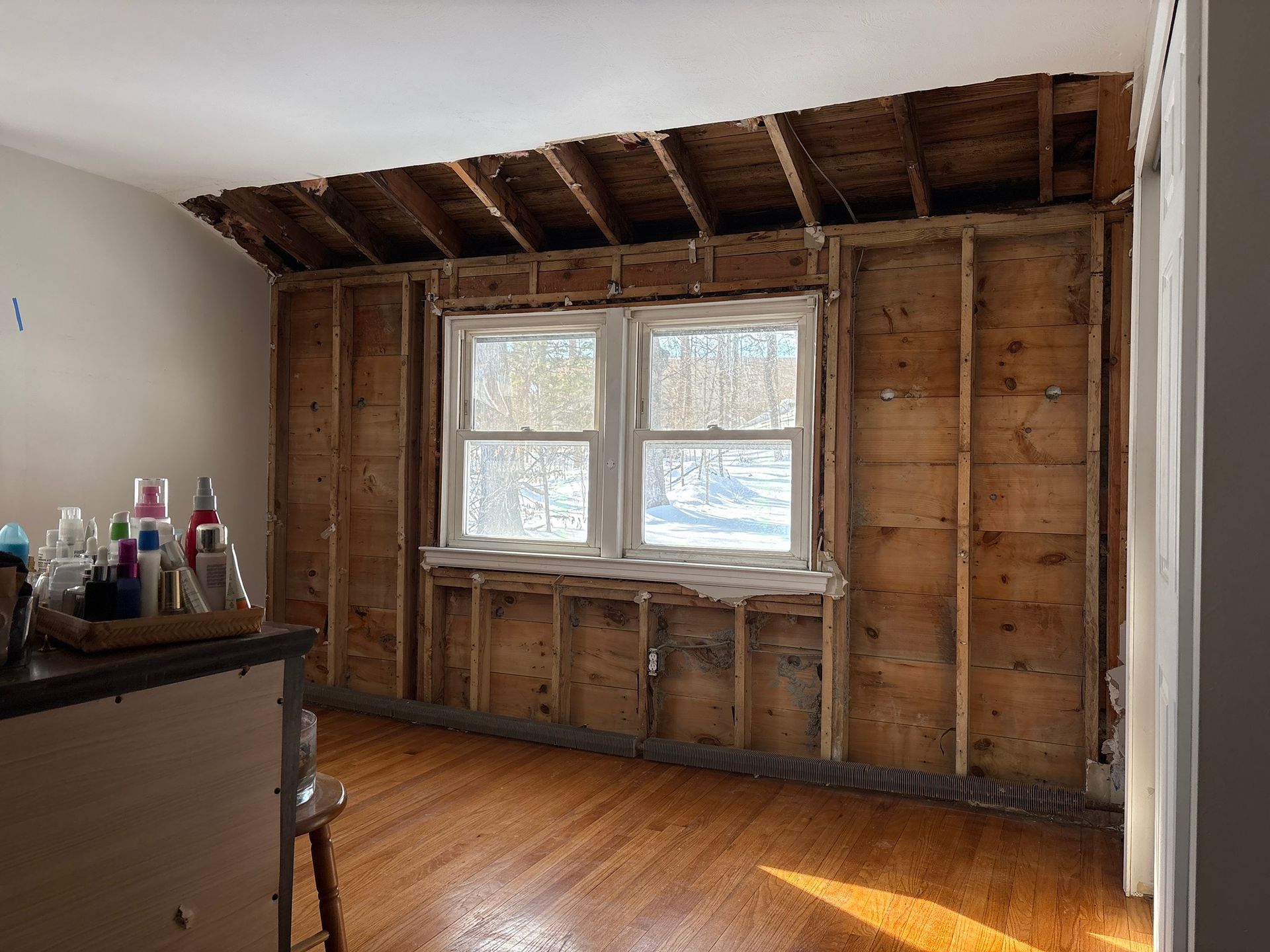 Empty room with exposed wall studs, a window, and wood flooring under renovation