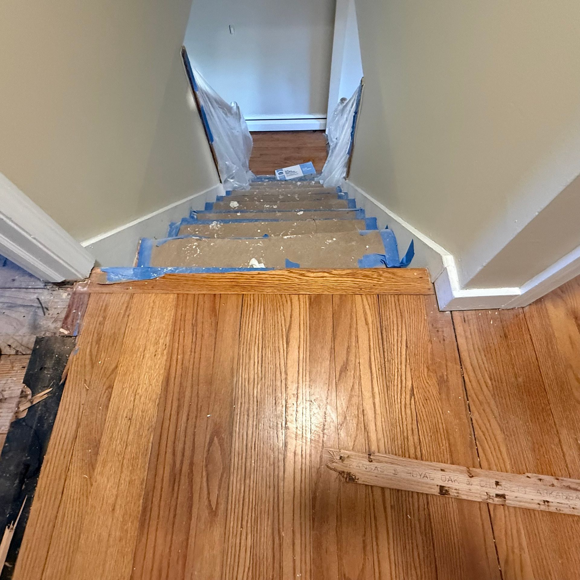Staircase under renovation with taped-down protective covering and exposed wood floor at the top landing