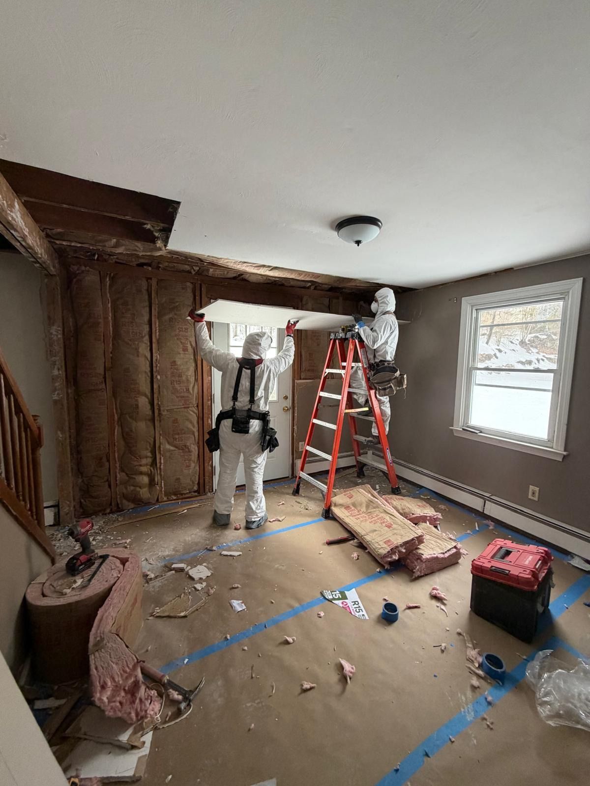 Home renovation with two workers, ladder, tools, and exposed wall framing in a room under construction.