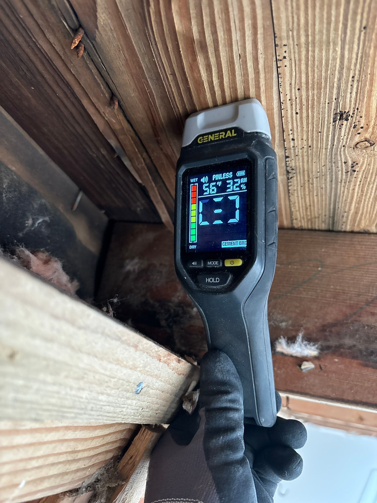 Handheld thermal camera inspecting a wooden beam and ceiling corner in a dim crawlspace