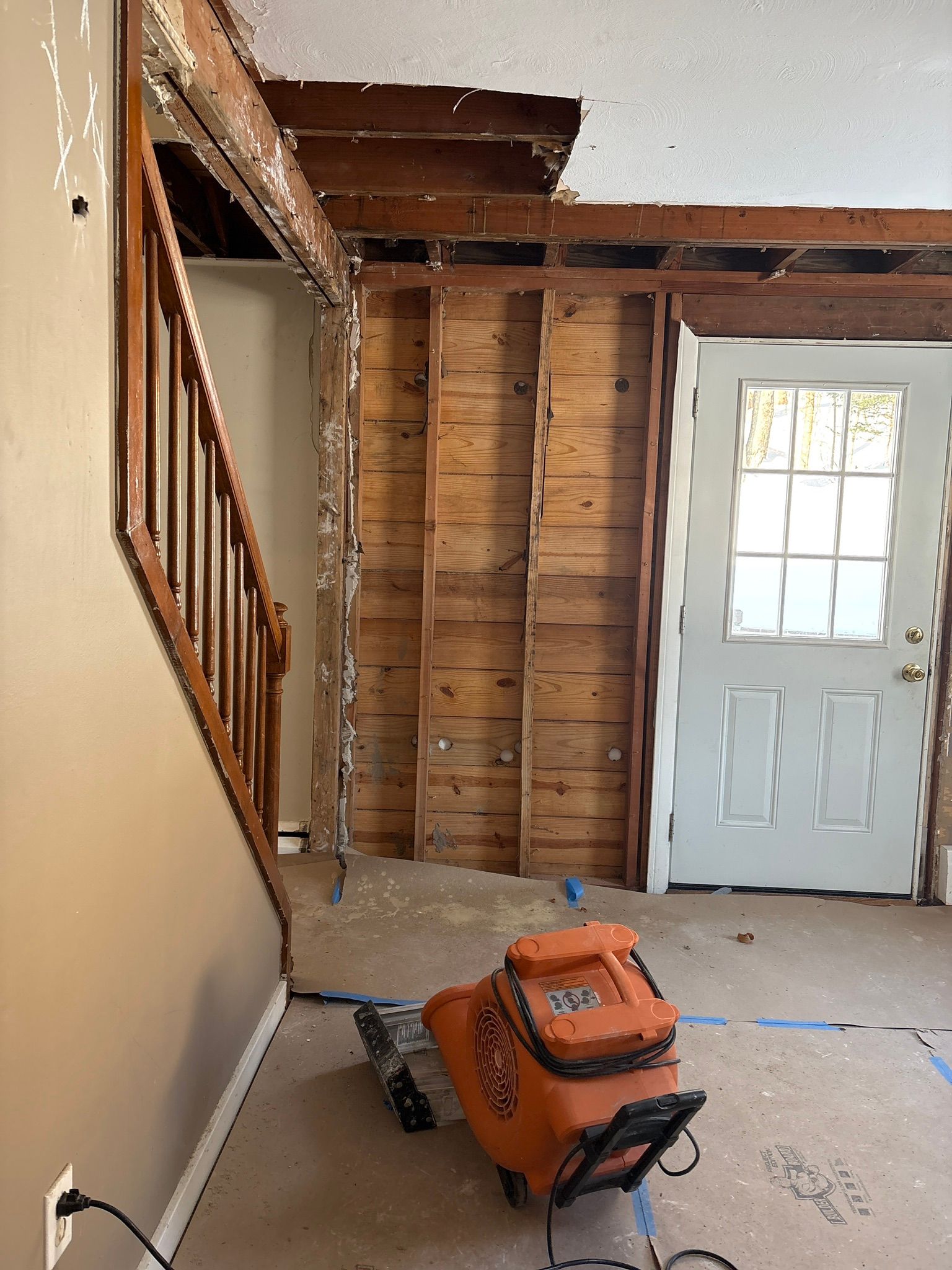 Partially renovated room with exposed studs, stairs, a white door, and an orange shop vacuum on the floor