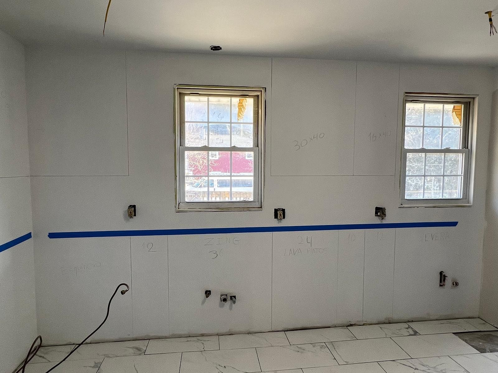 Unfinished kitchen wall with two windows, blue tape line, exposed outlets, and electrical wires
