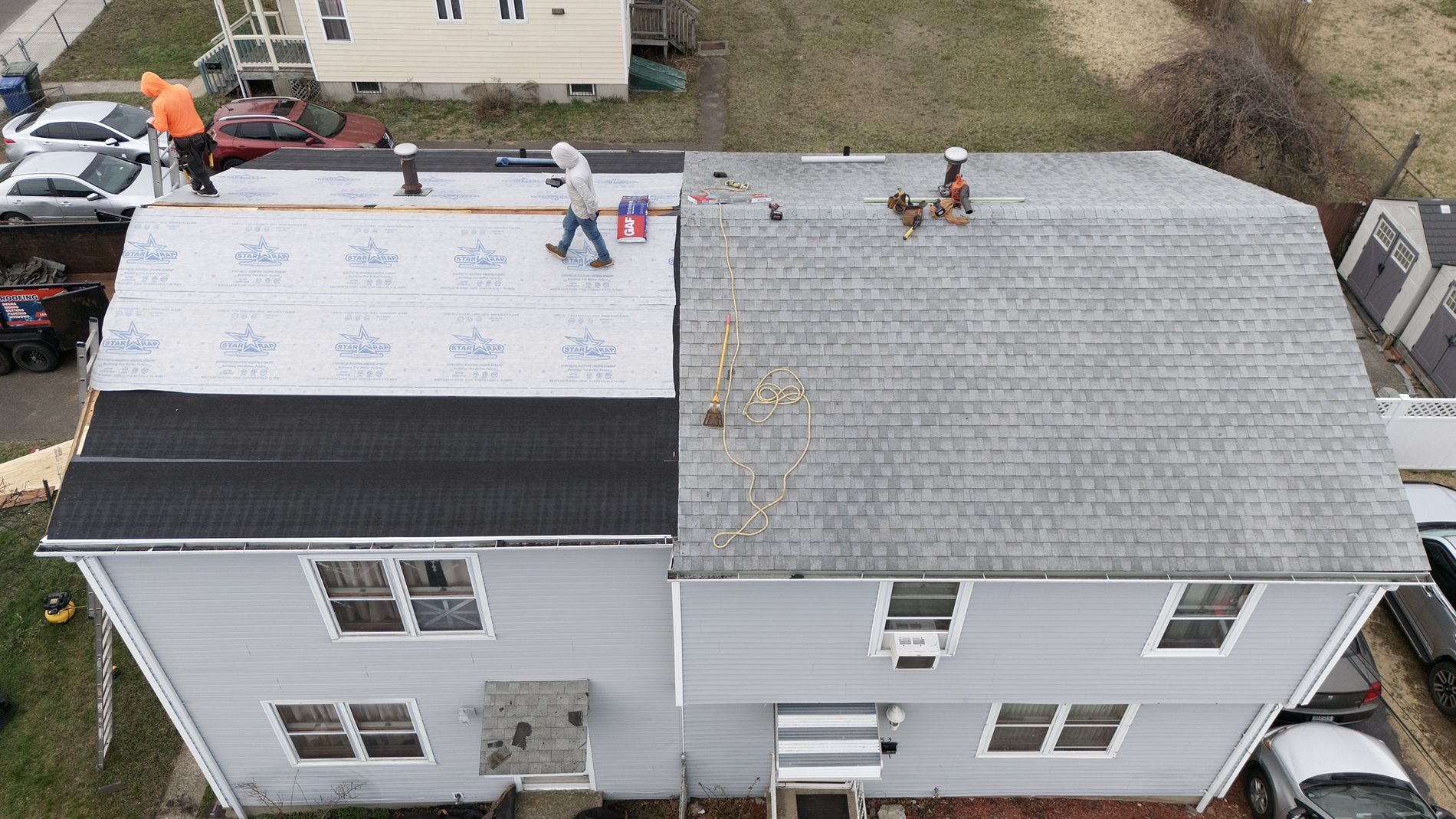 Aerial view of workers installing a new roof on a two-story house, with one side covered in white underlayment.