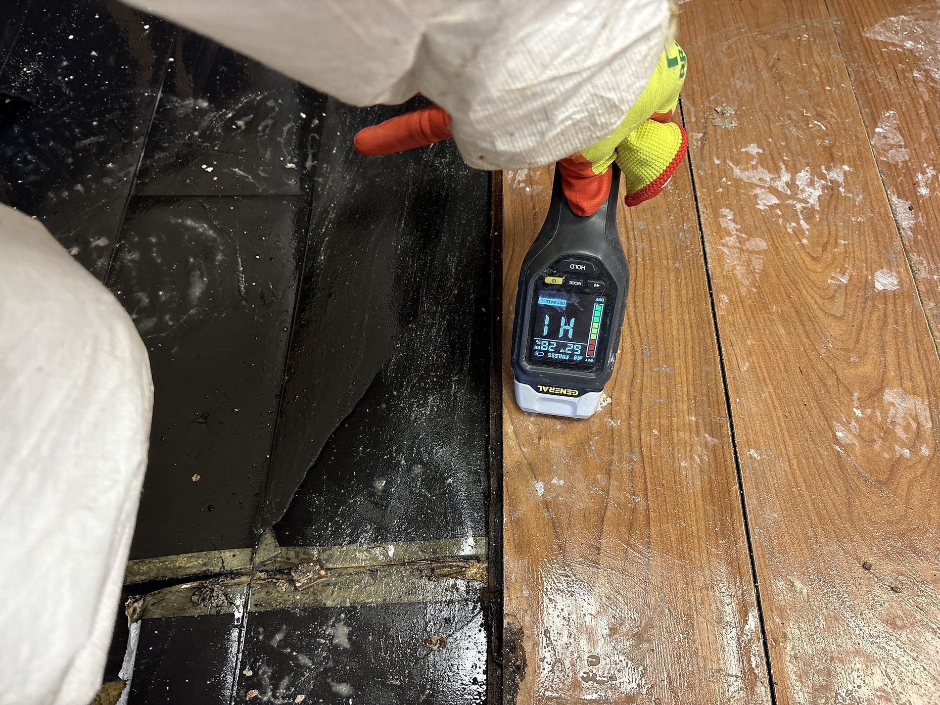 Person using a handheld dust meter beside a black couch and wood floor scattered with white powder