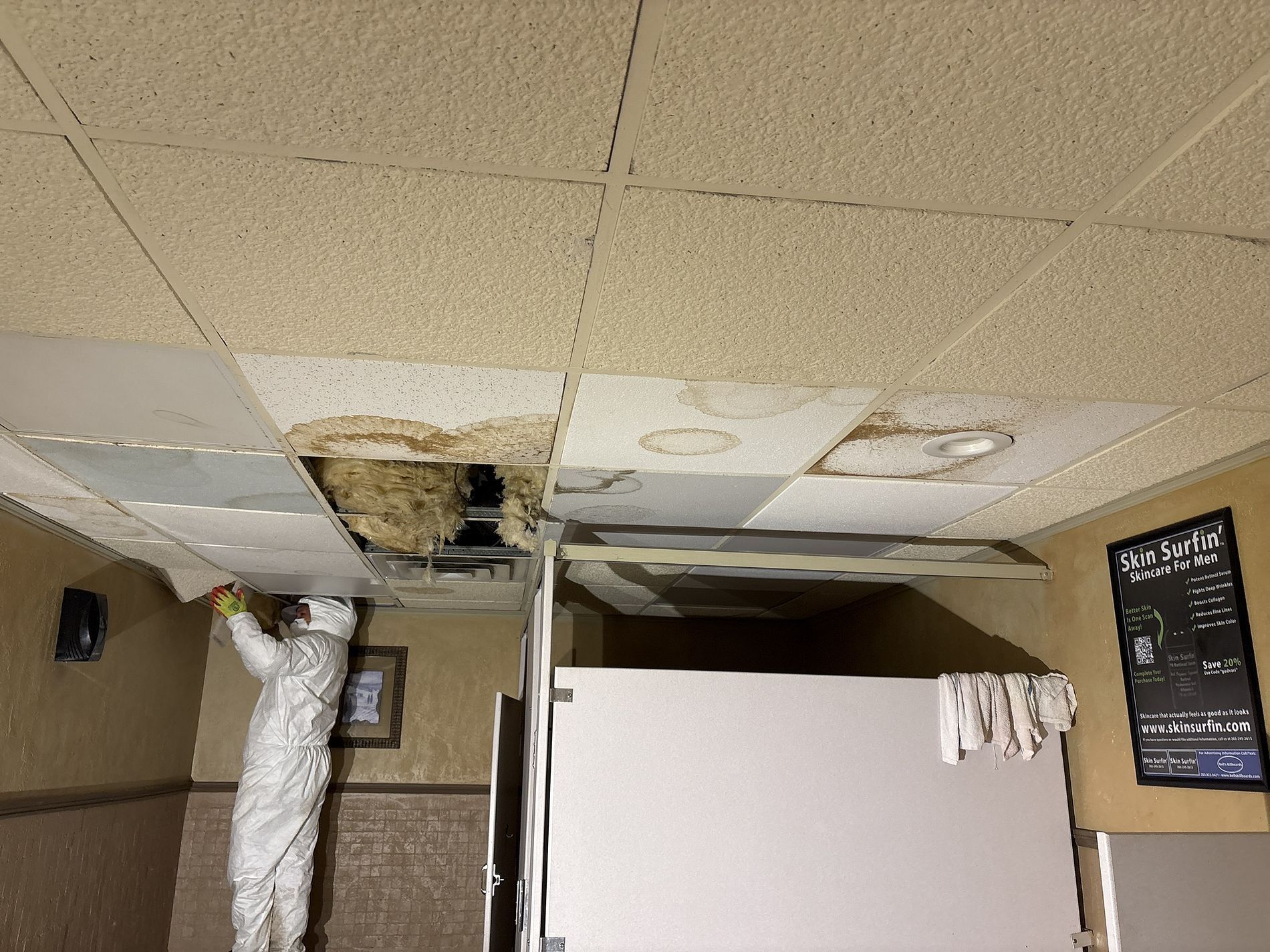 Damaged ceiling with missing tiles and exposed ductwork in an indoor room with a partial wall divider