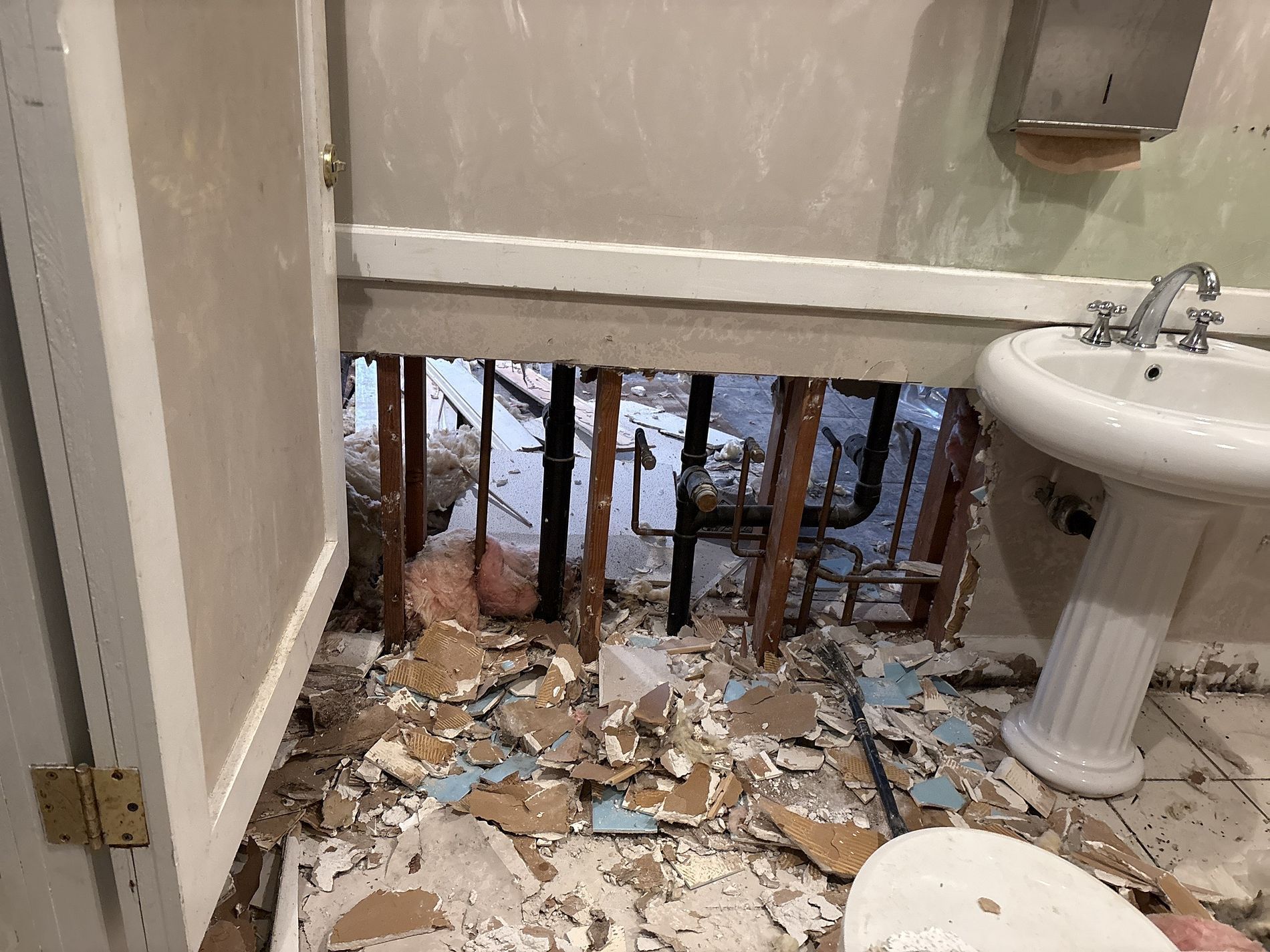 Bathroom floor collapsed into a hole, with broken debris and exposed joists near the sink.