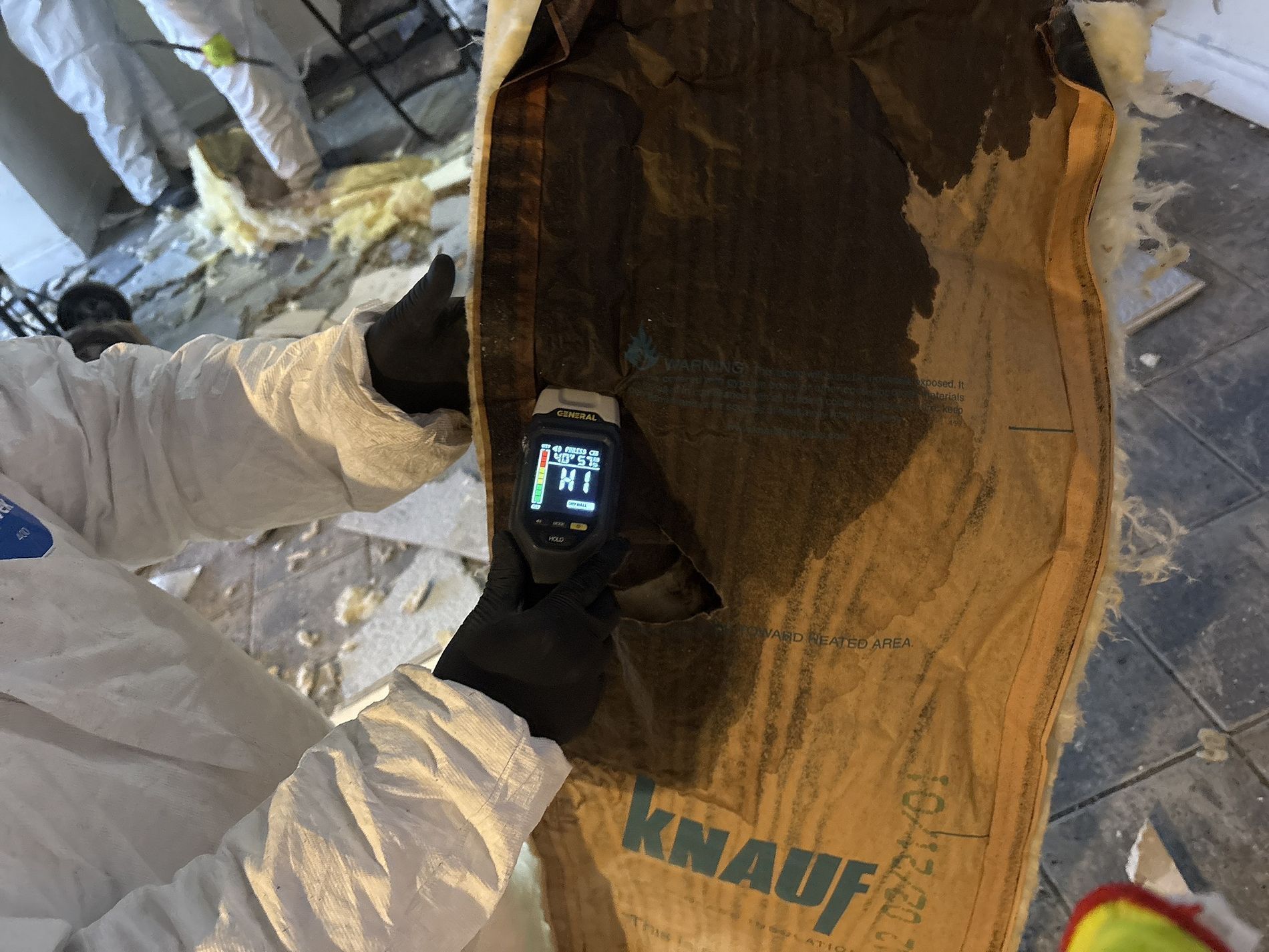 Worker using a handheld thermal camera to inspect insulation inside a wall cavity