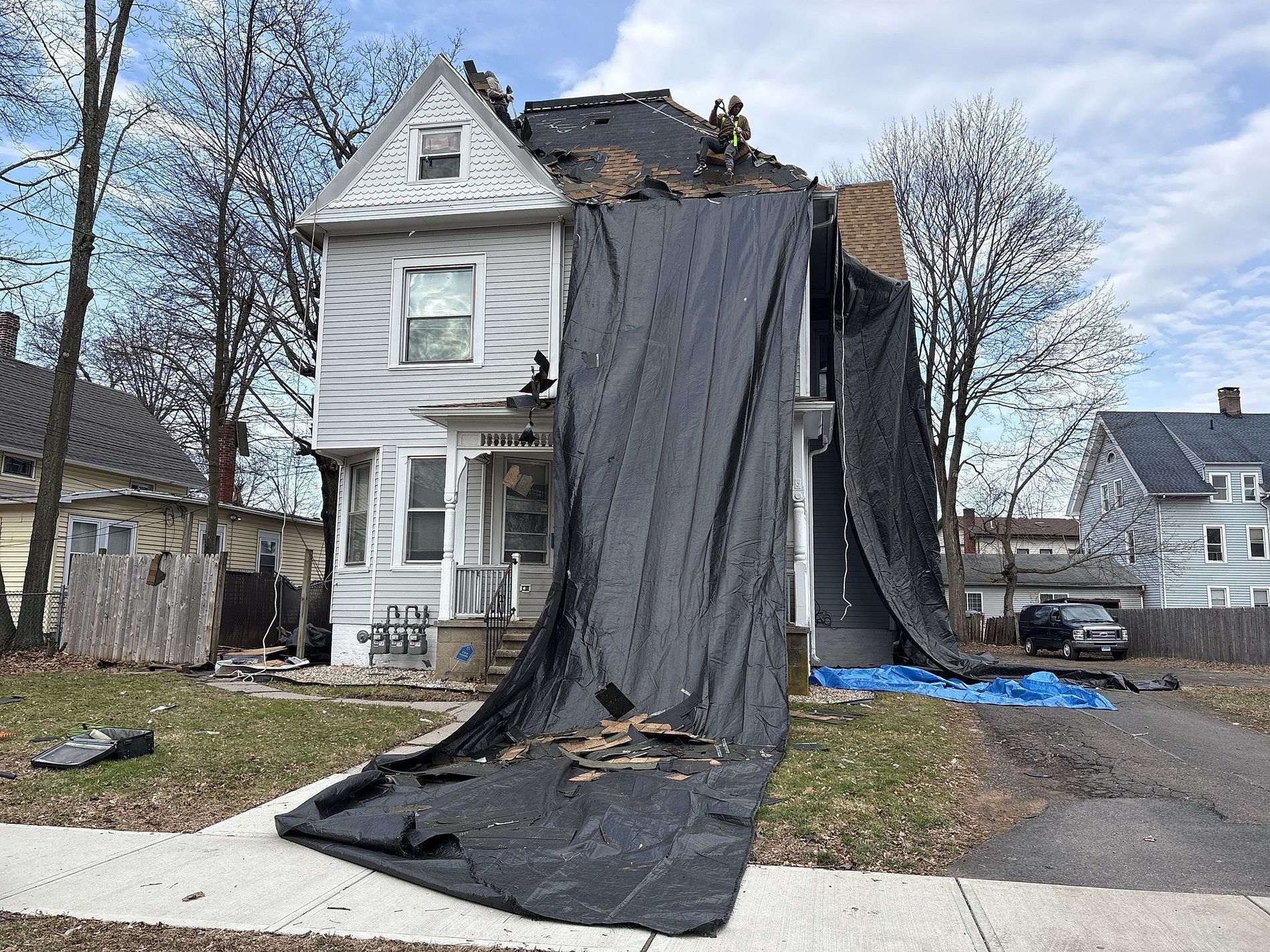 Damaged white house with a large black tarp draped over the front after roof damage