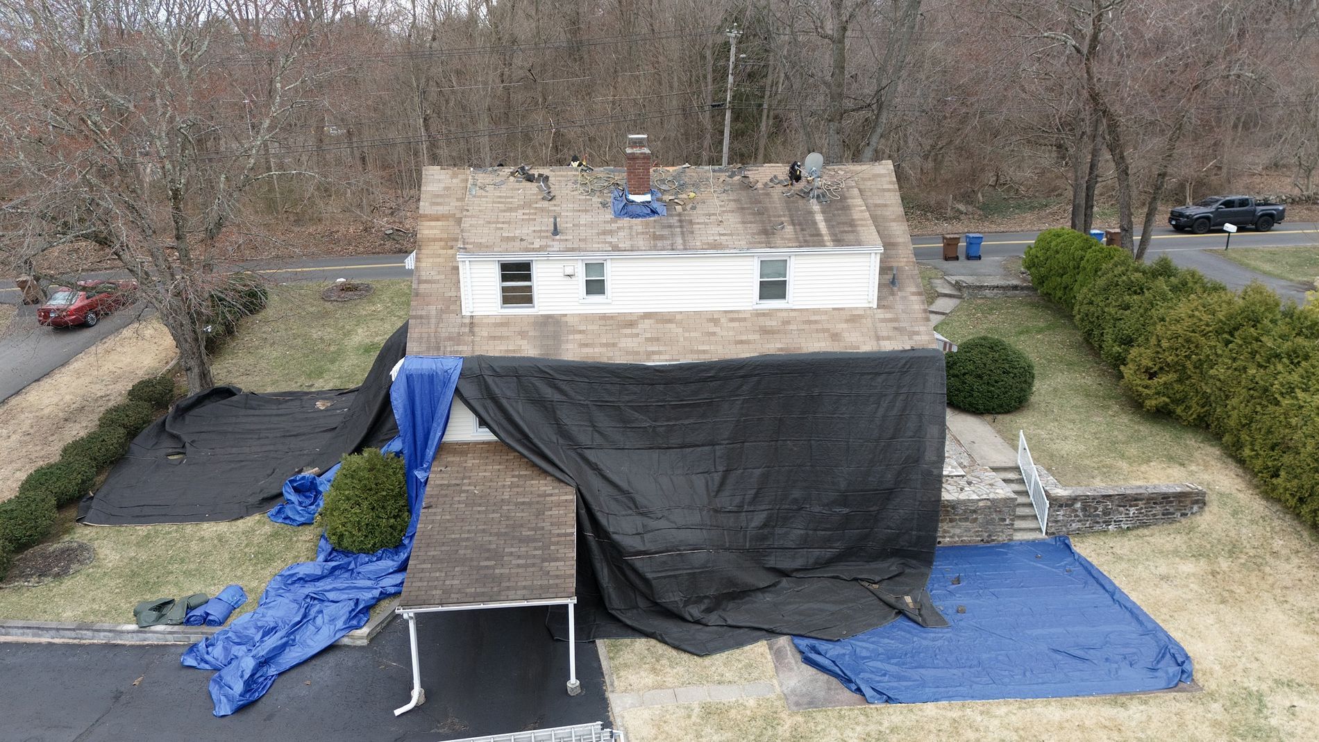 Makeshift shelter with blue tarps and black cover in a yard, viewed from above