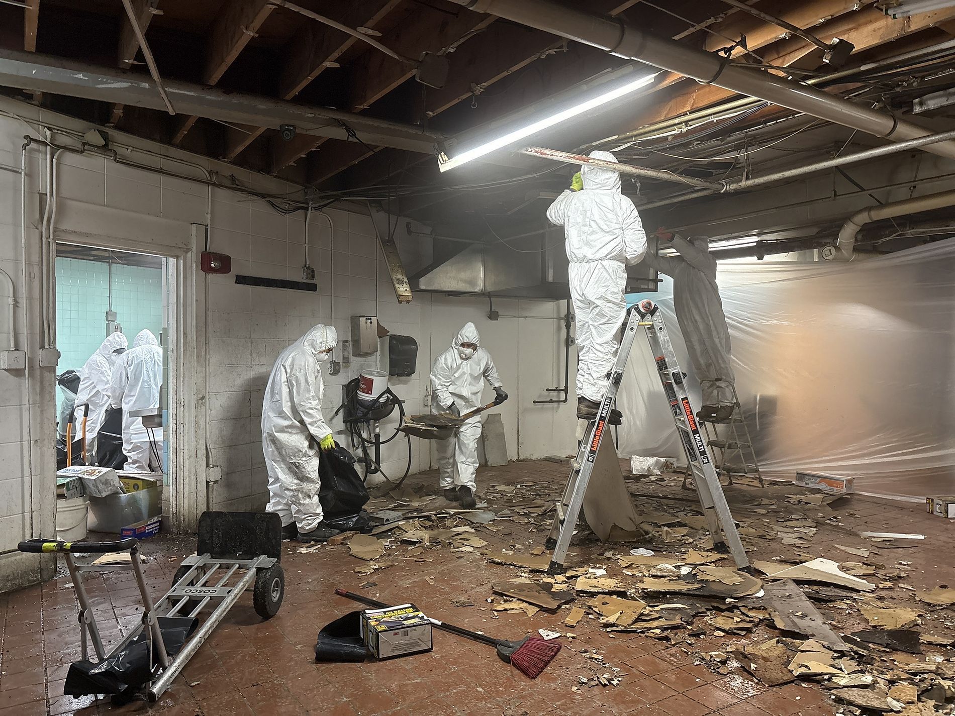 Workers in hazmat suits cleaning debris inside a damaged building interior