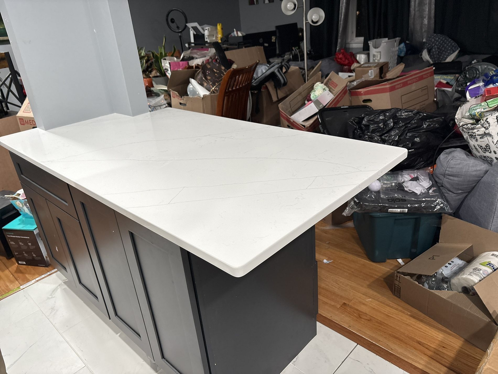 White kitchen island with cabinets in a cluttered room with boxes and scattered items.