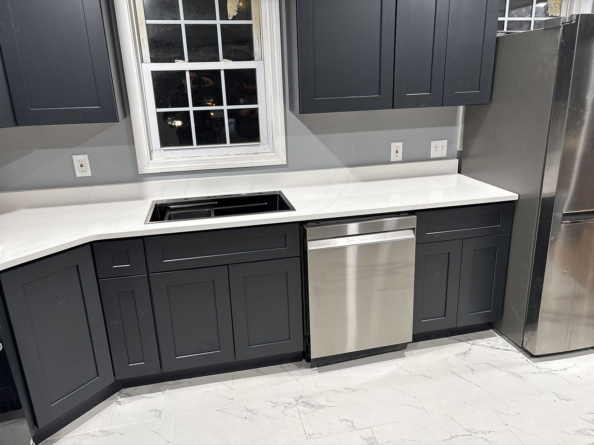 Modern kitchen with dark cabinets, white countertops, stainless dishwasher, and large stainless refrigerator