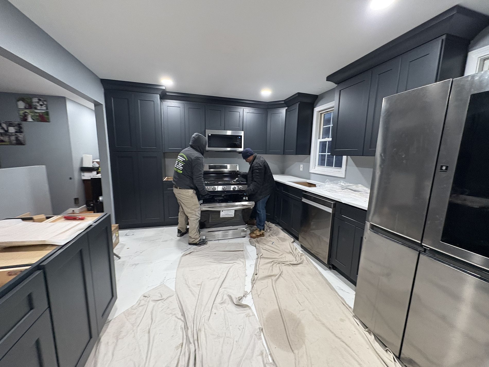 Person working in a sleek black-and-stainless-steel kitchen with marble-look floor and countertops
