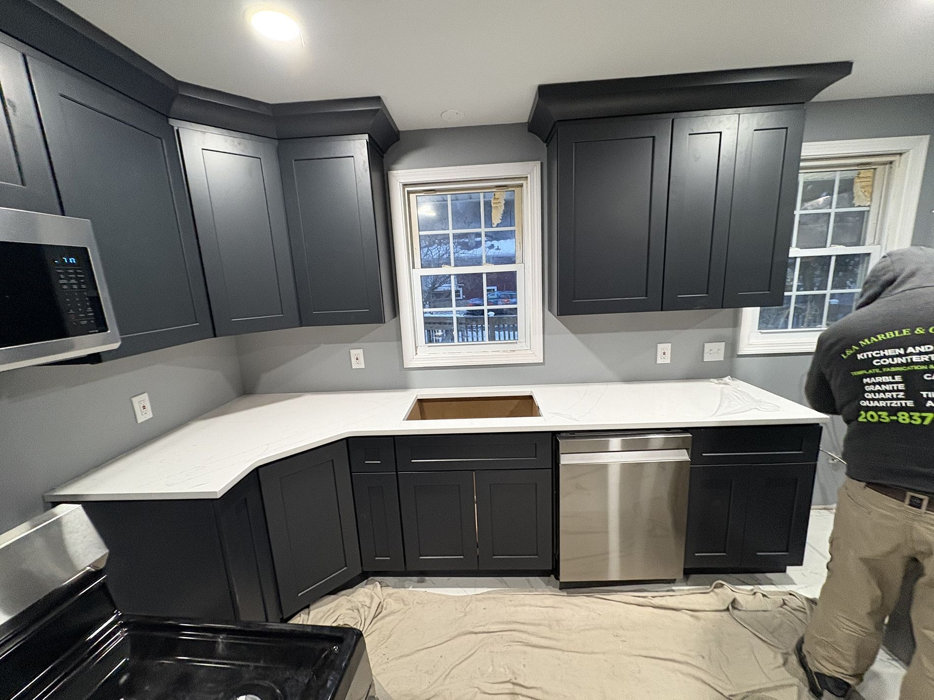 Modern kitchen with dark cabinets, white countertops, stainless dishwasher, and two windows