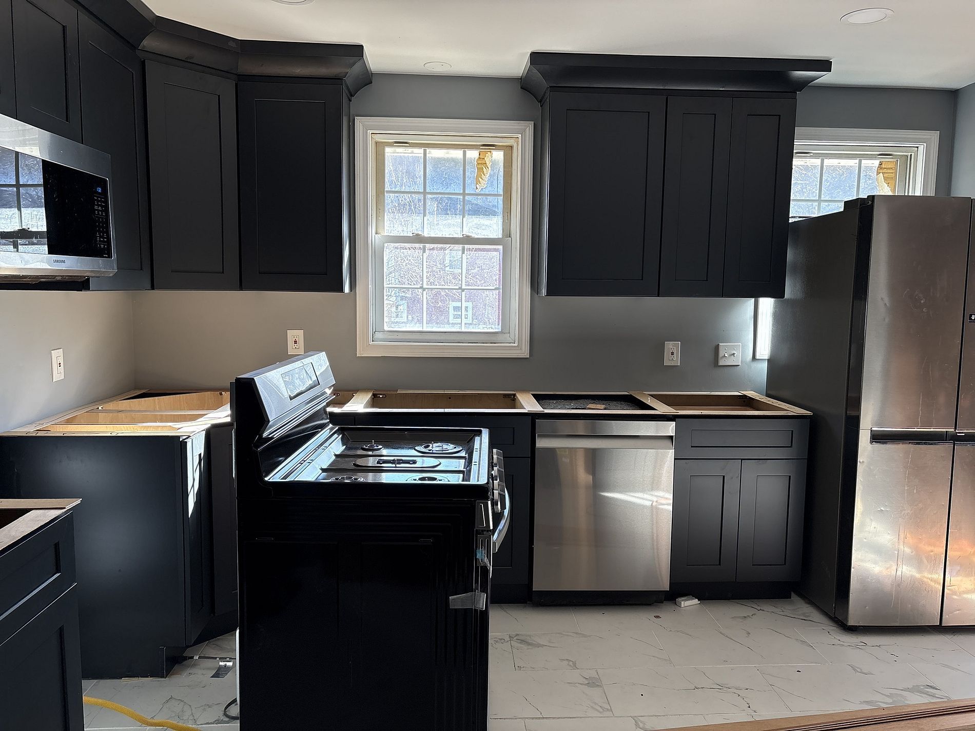 Modern kitchen with dark cabinets, stainless fridge, stove, dishwasher, and a window above the sink.