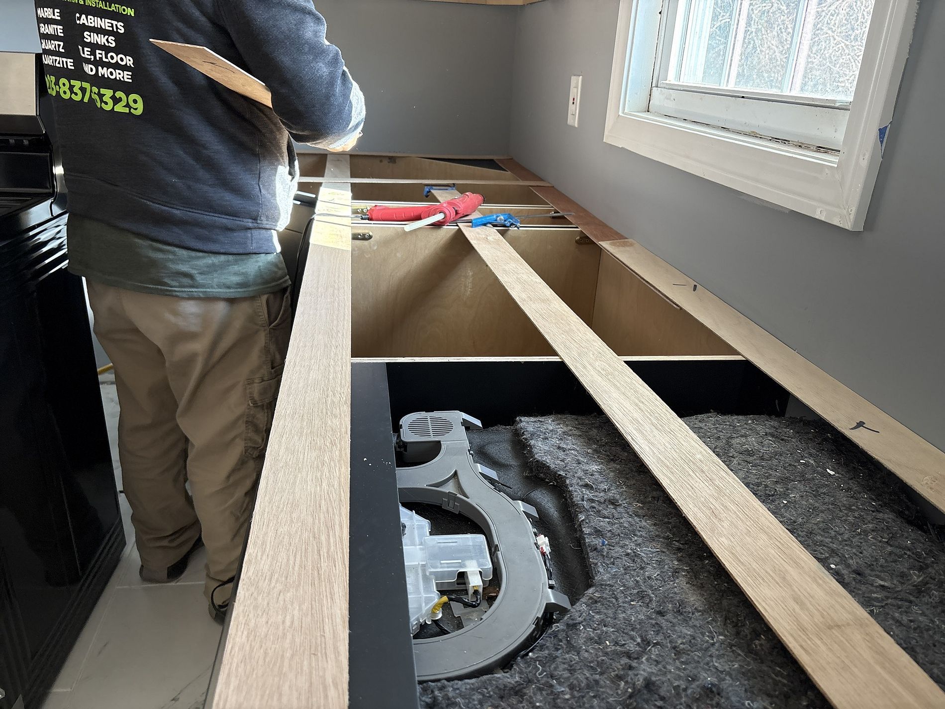 Person assembling wooden framing over a floor opening in a room with windows.