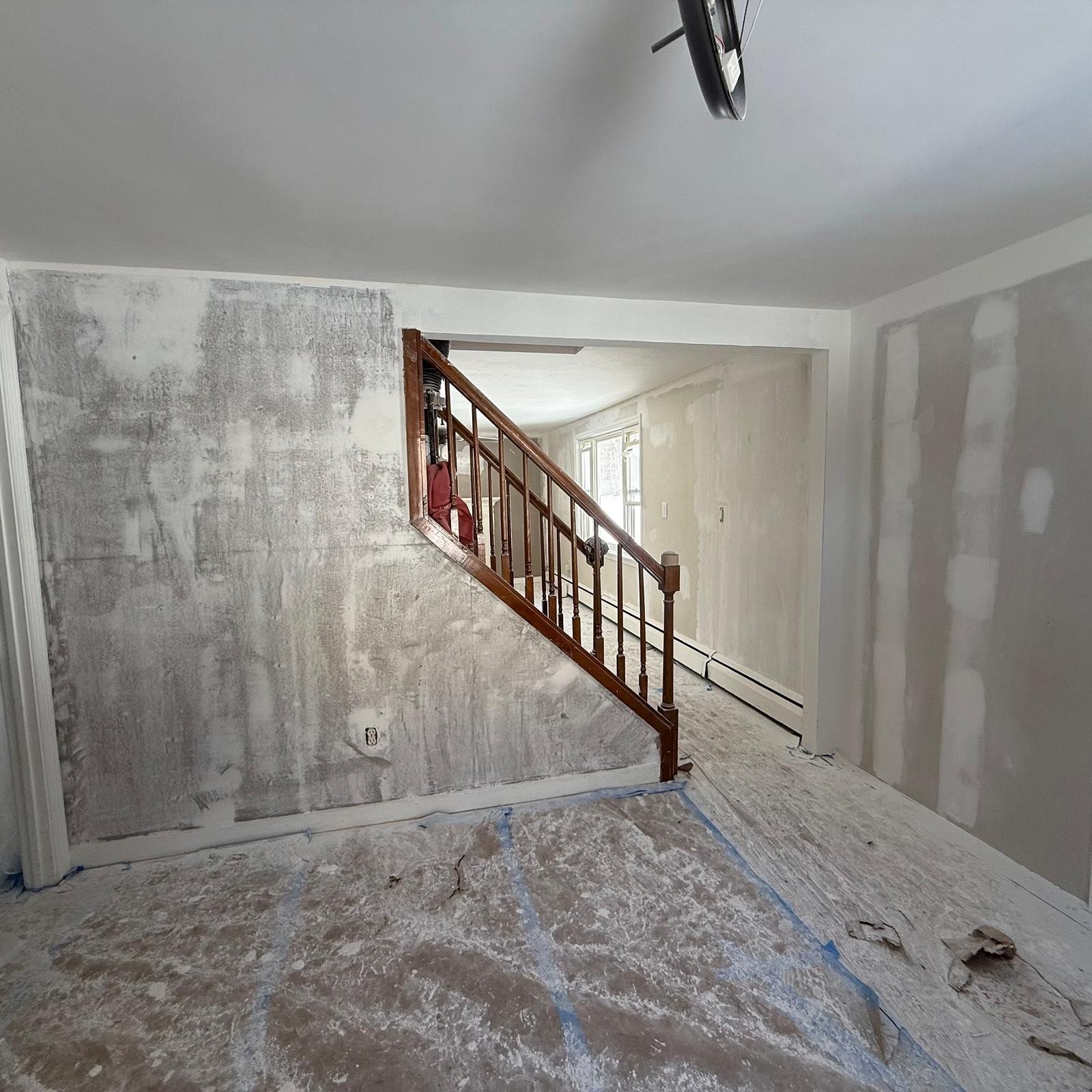 Partially renovated room with stairs, drywall patches, and drop cloths on the floor